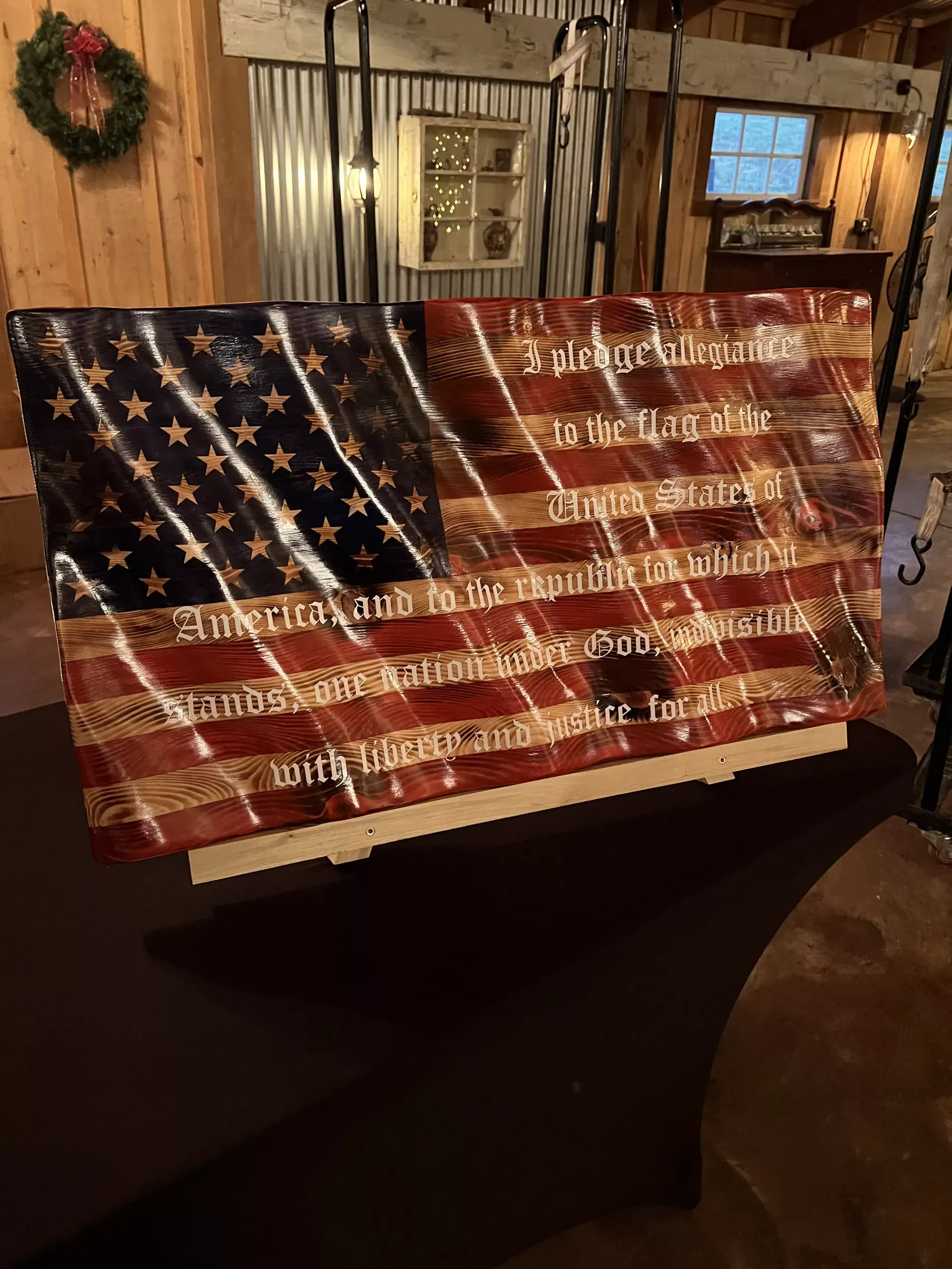 Patriotic American flag sign with white text displayed indoors on a wooden stand.