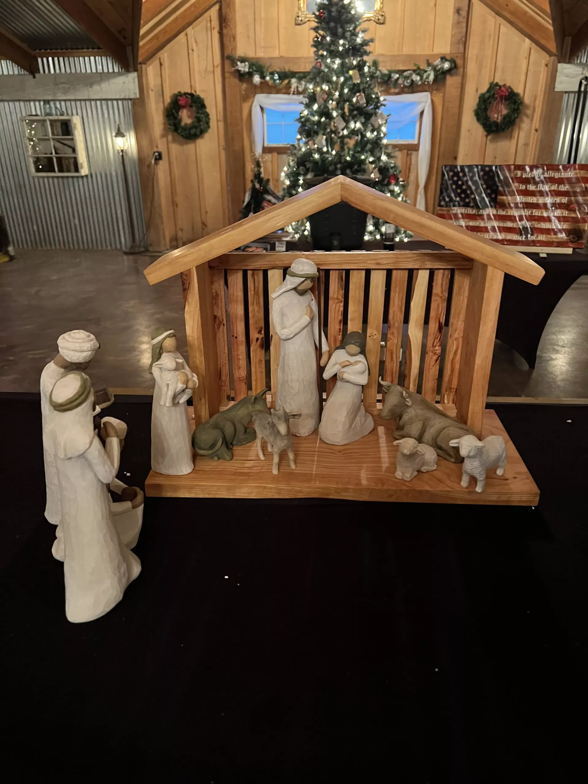 Nativity scene with Mary, Joseph, baby Jesus, and animals in a wooden stable, lit by a Christmas tree