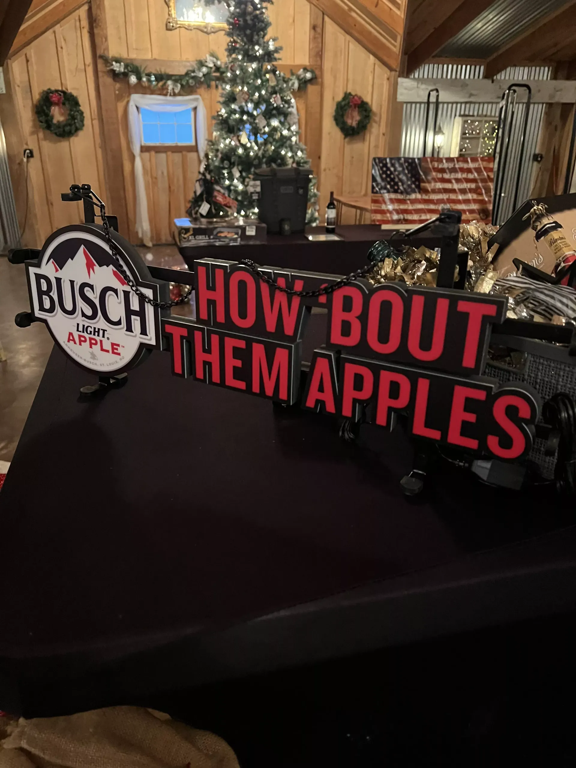 Busch sign saying “How ’Bout Them Apples” on a table in a cozy decorated room with a lit Christmas tree