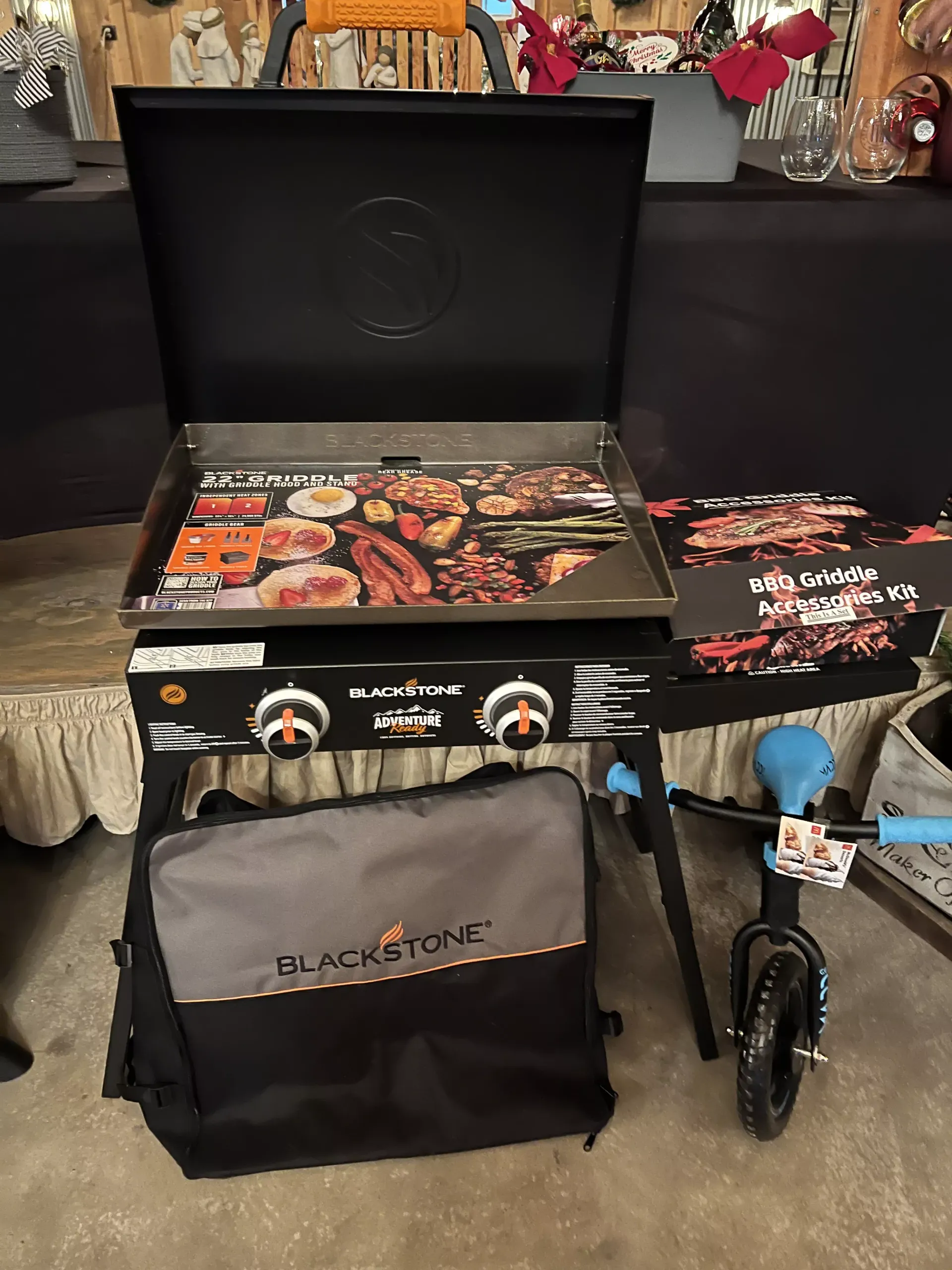 Blackstone griddle with open lid, cooking accessories, and wheeled storage bag displayed on a table