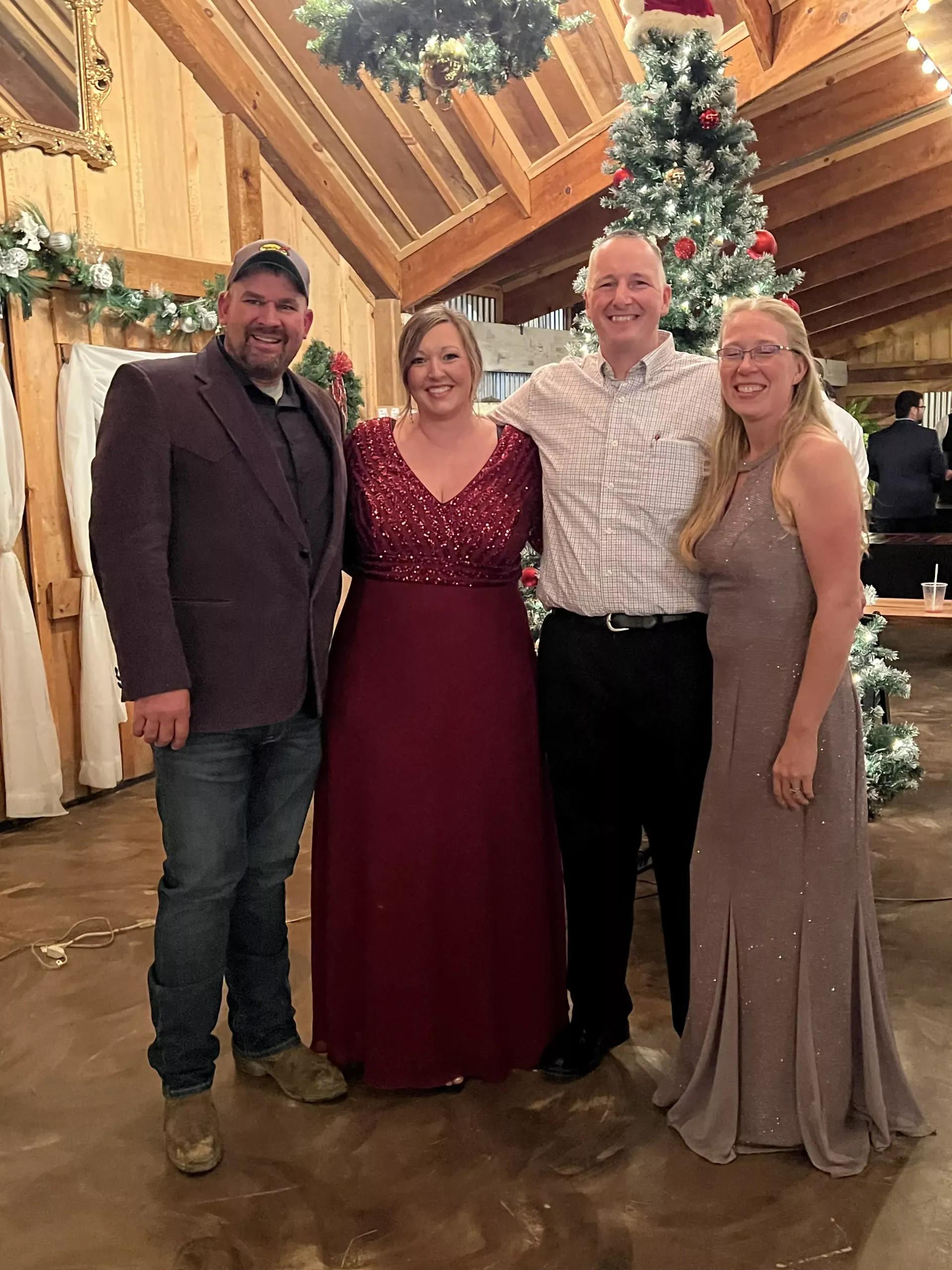 Four people posing together at a festive holiday event beside a decorated Christmas tree.