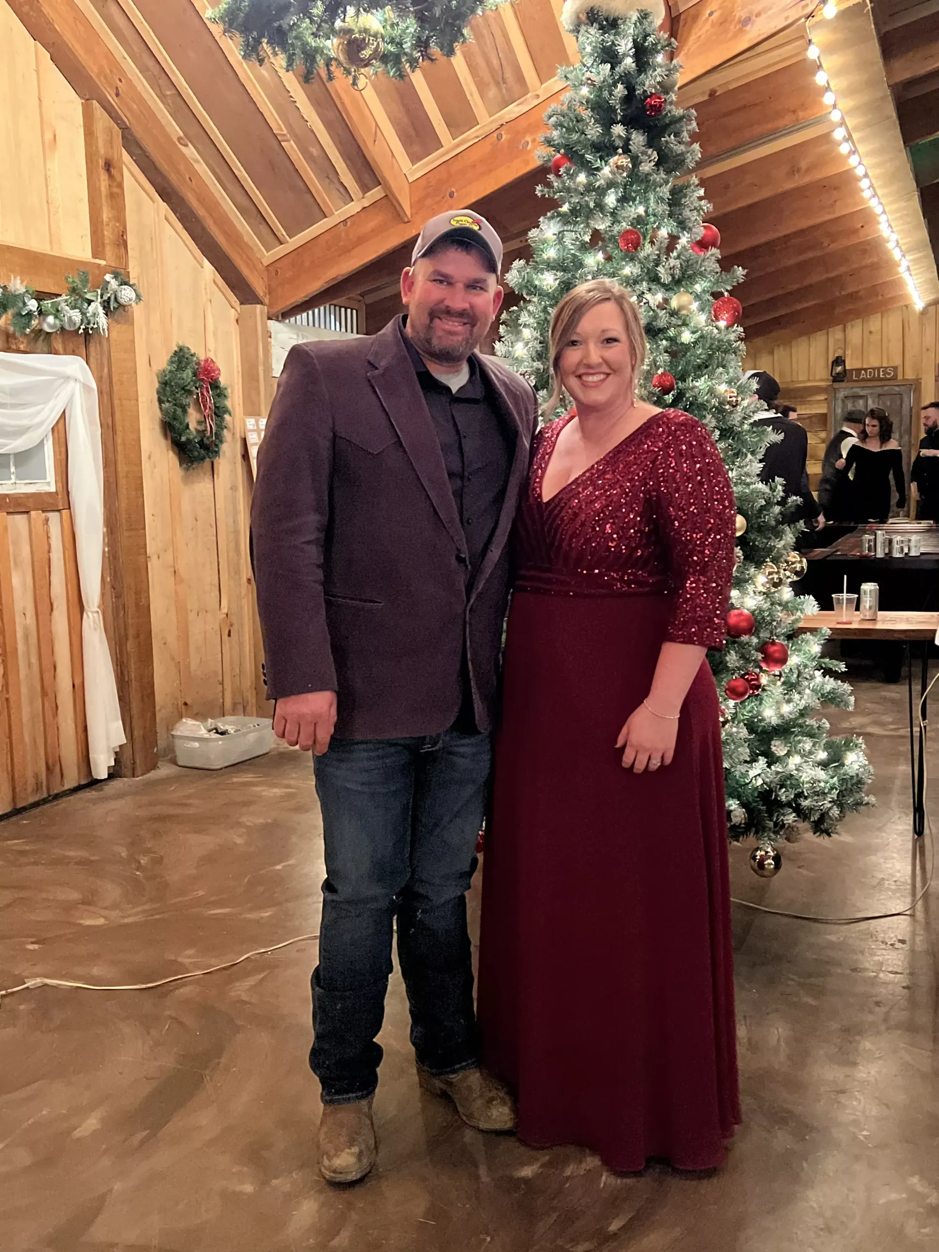 Couple posing in a wood-paneled hall beside a decorated Christmas tree
