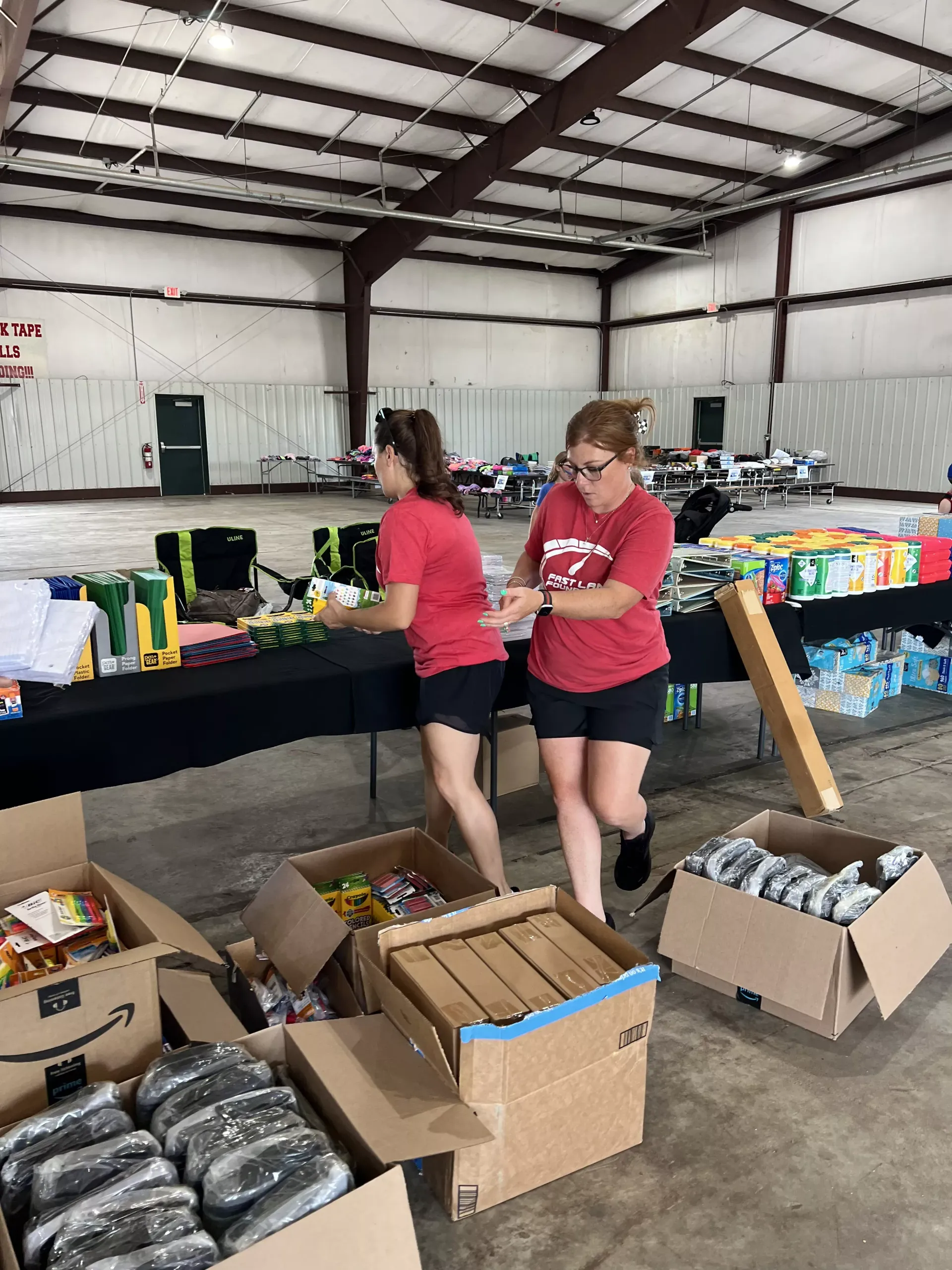 Volunteers sorting supplies at tables in a warehouse, with boxes of canned goods in the foreground