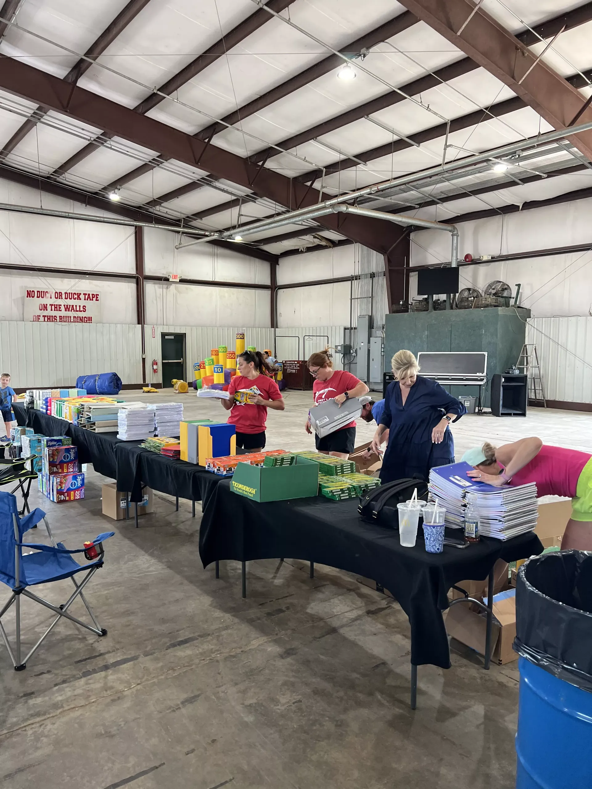 People sorting donations at tables in a large indoor warehouse with bins and supplies