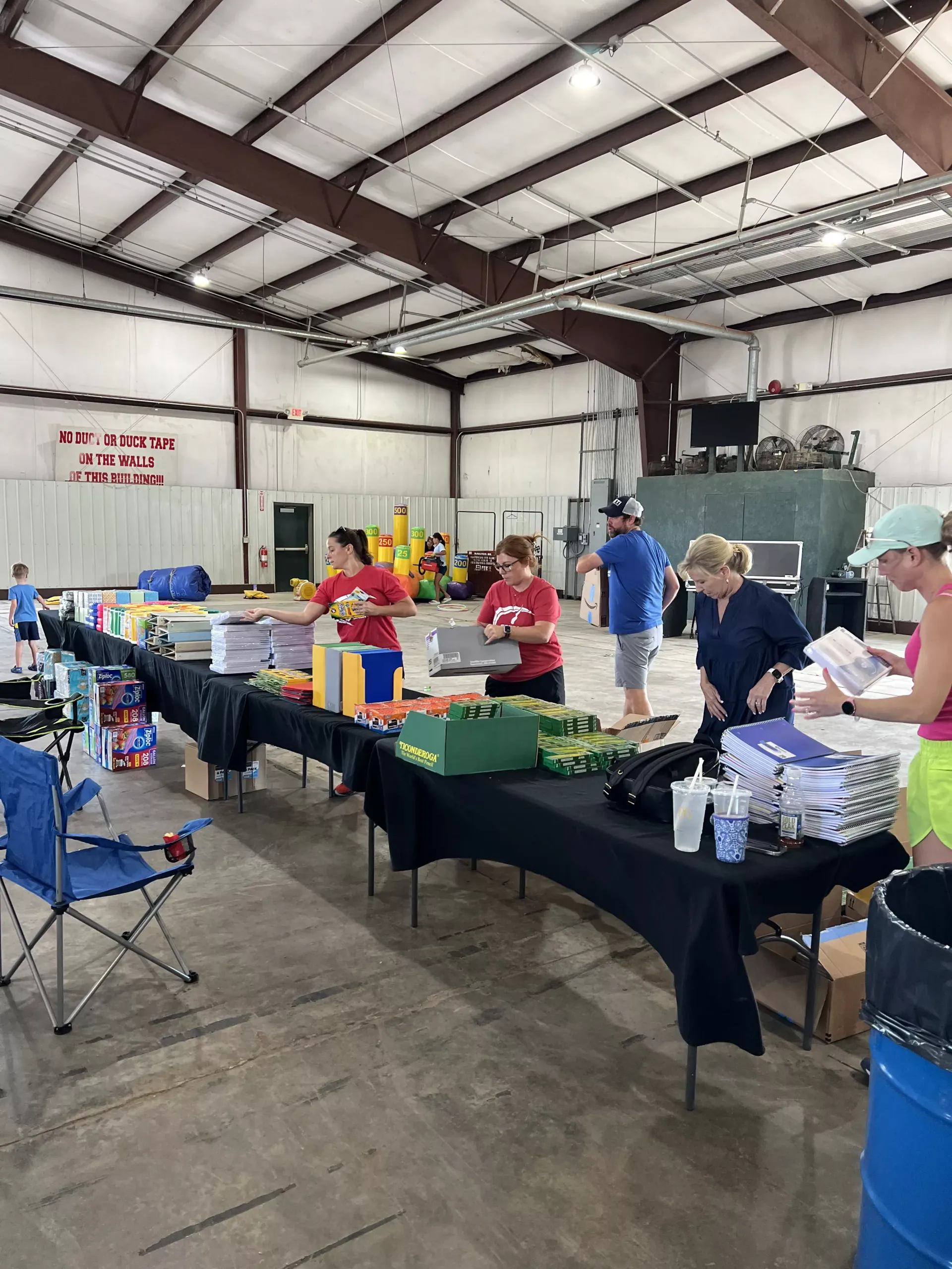 Volunteers sorting donations at tables inside a warehouse, with boxes and supplies around them.