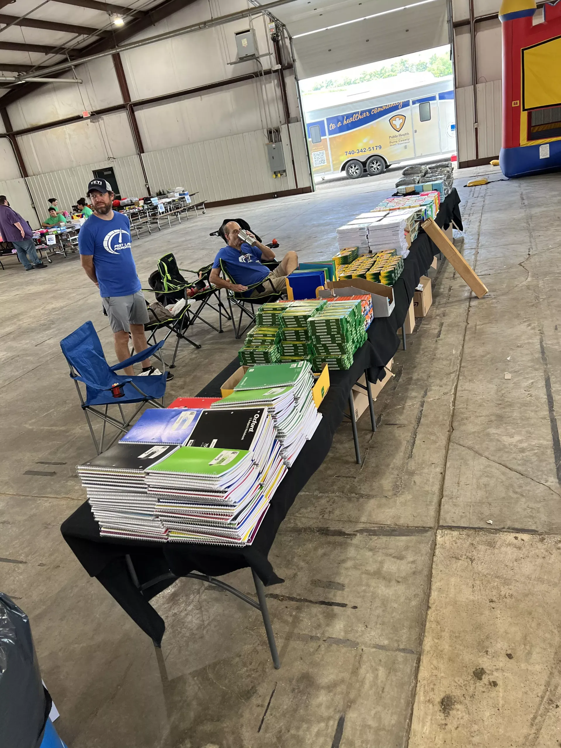 Vendor tables with books and items in a large indoor hall, with a few people nearby