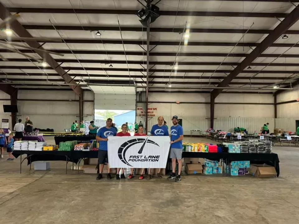 People standing behind a table at an indoor donation or outreach event with boxes and supplies.