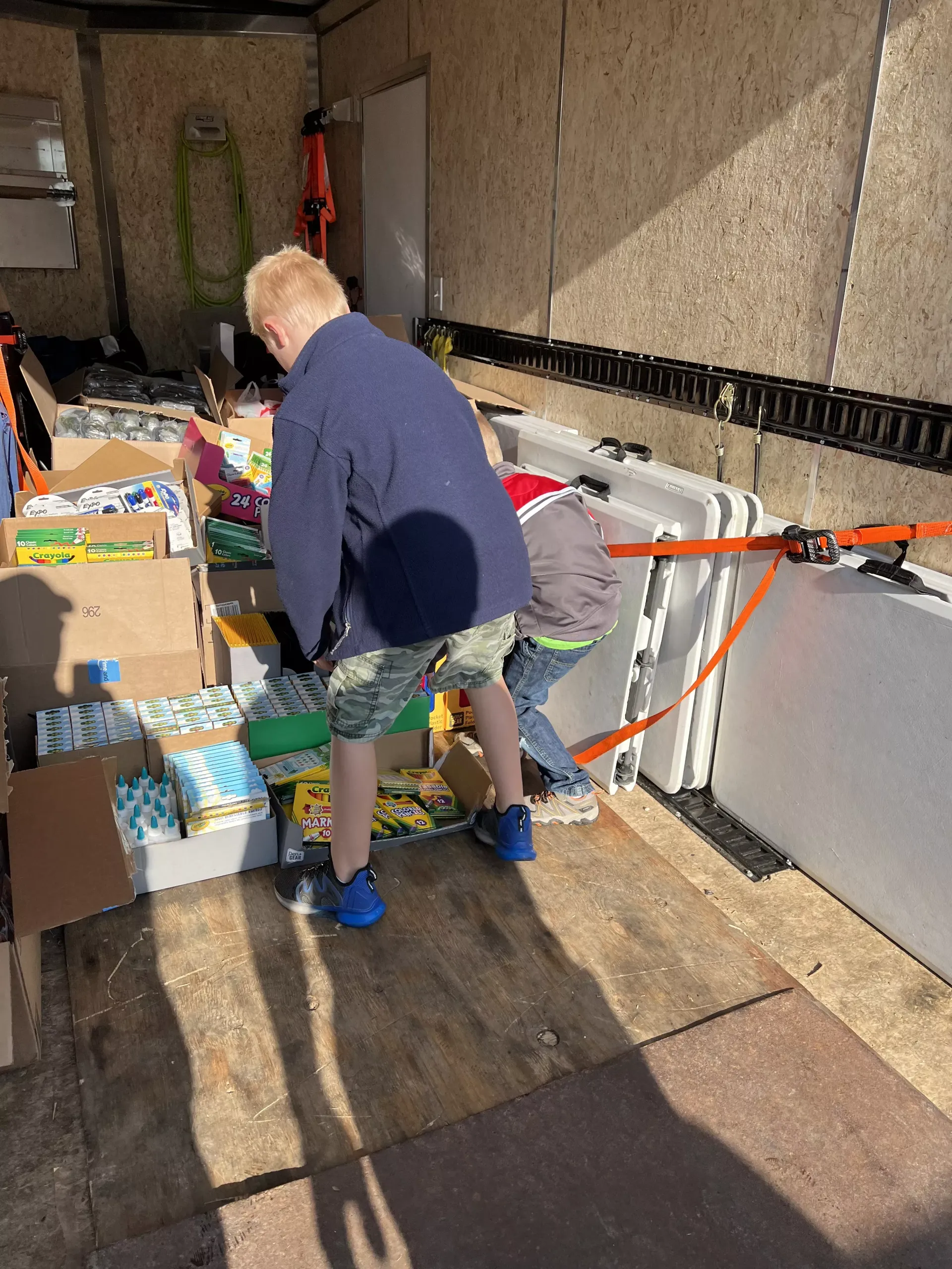 Two people unload boxes from a truck in bright sunlight.