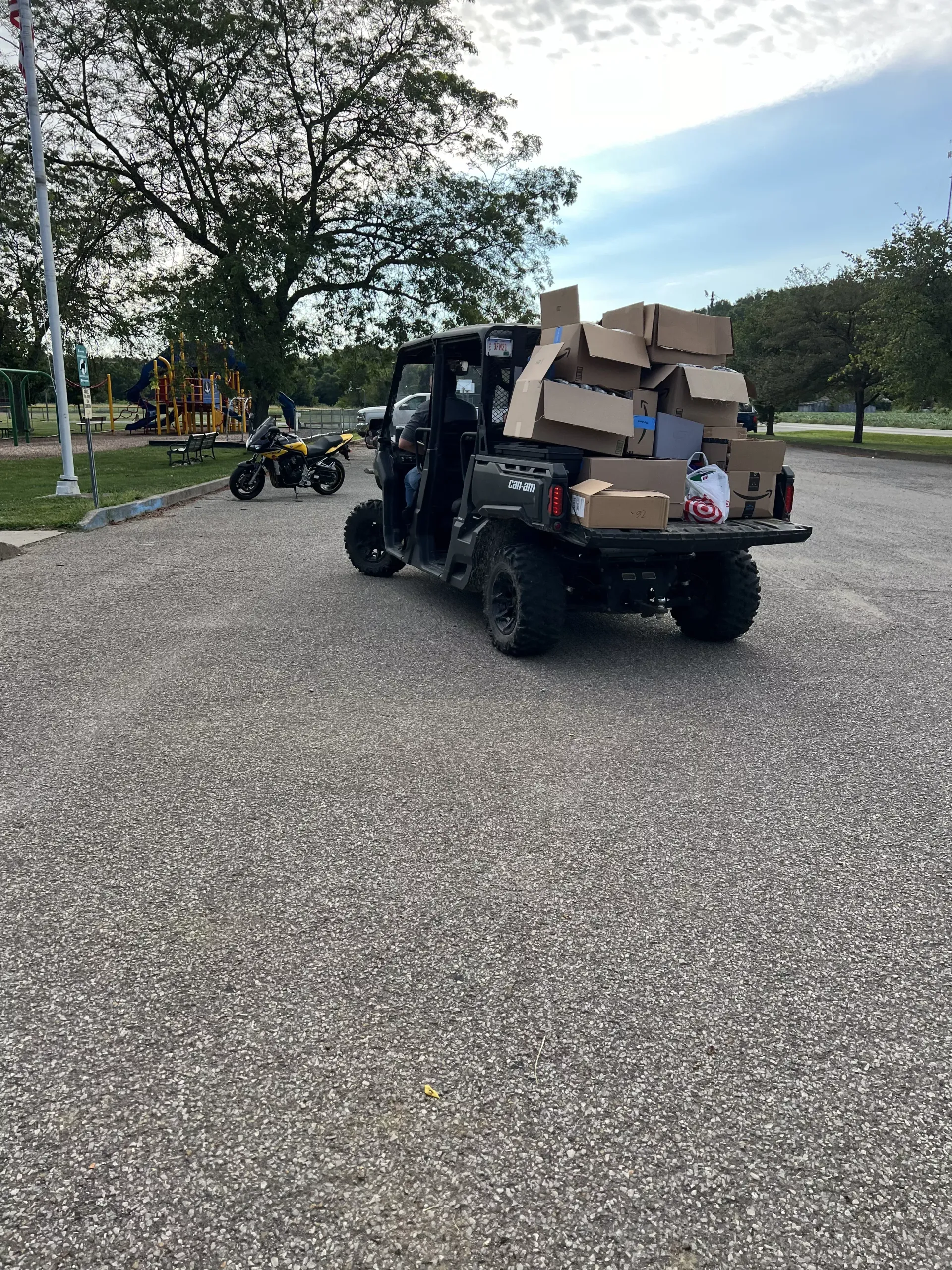 Black utility vehicle loaded with stacked cardboard boxes on a gravel path in a park