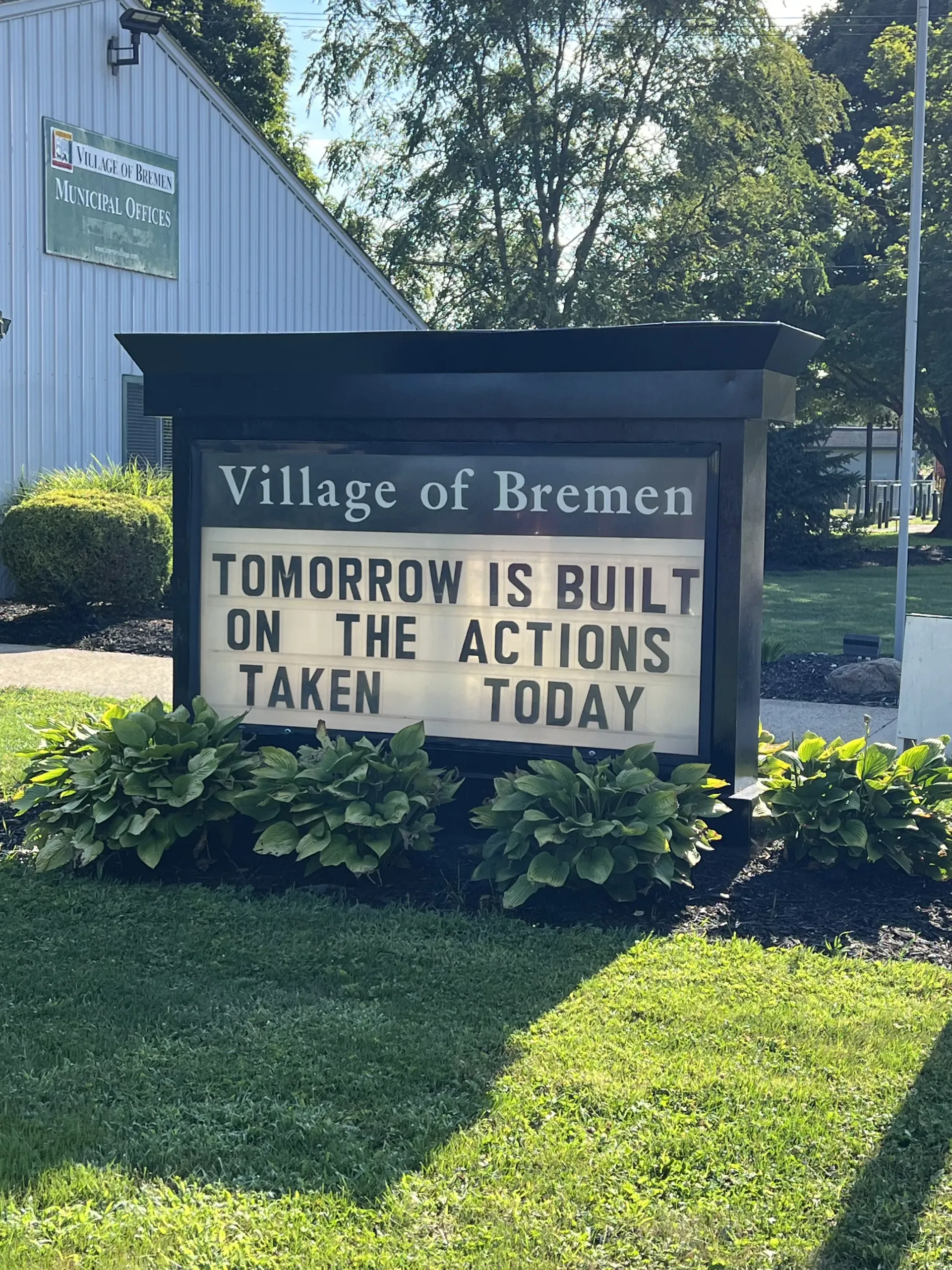 Village of Bremen sign reading, “Tomorrow is built on the actions taken today,” beside a building and trees