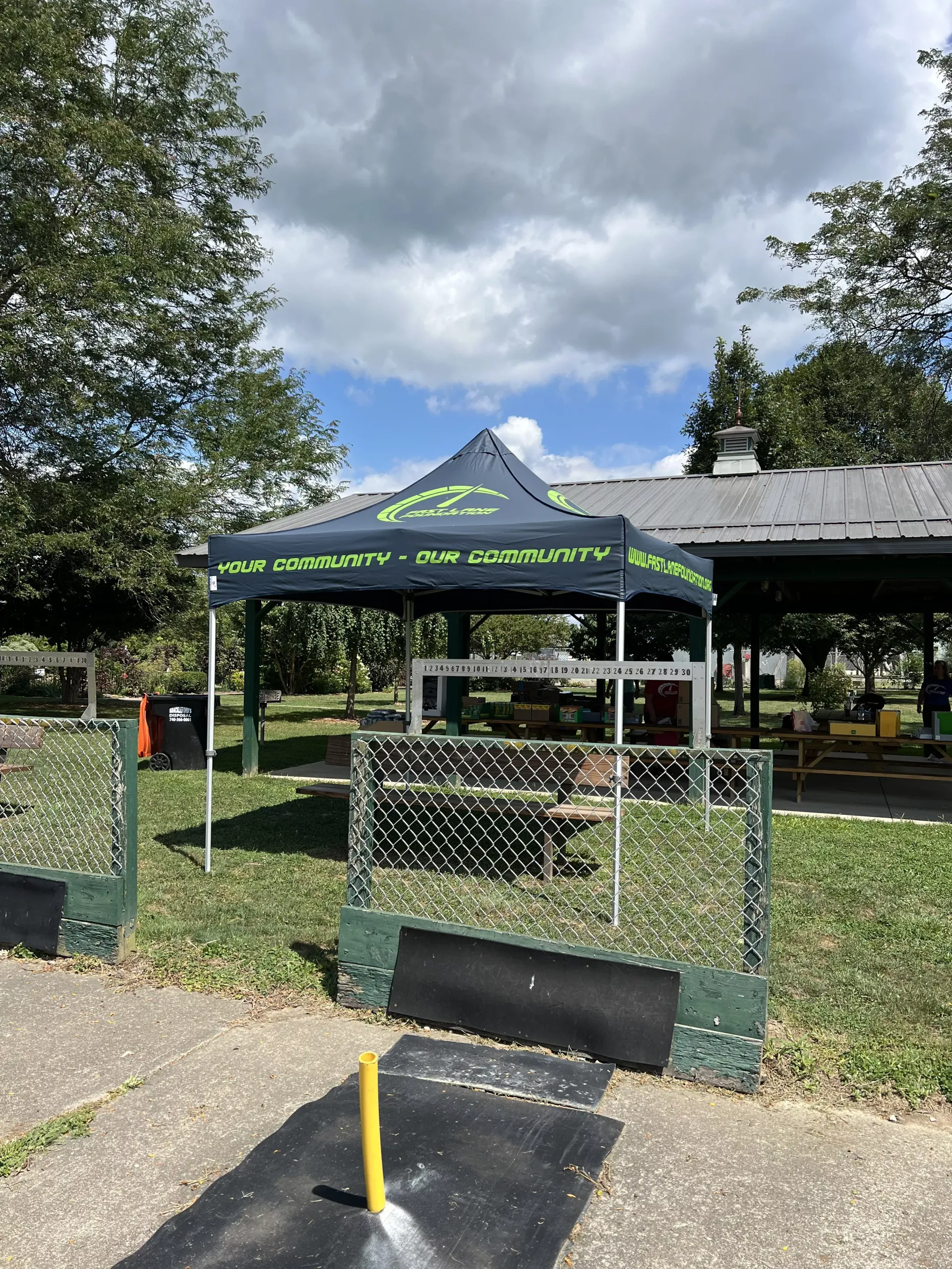 Black canopy tent at a fenced outdoor entrance, with a paved path and cloudy sky.
