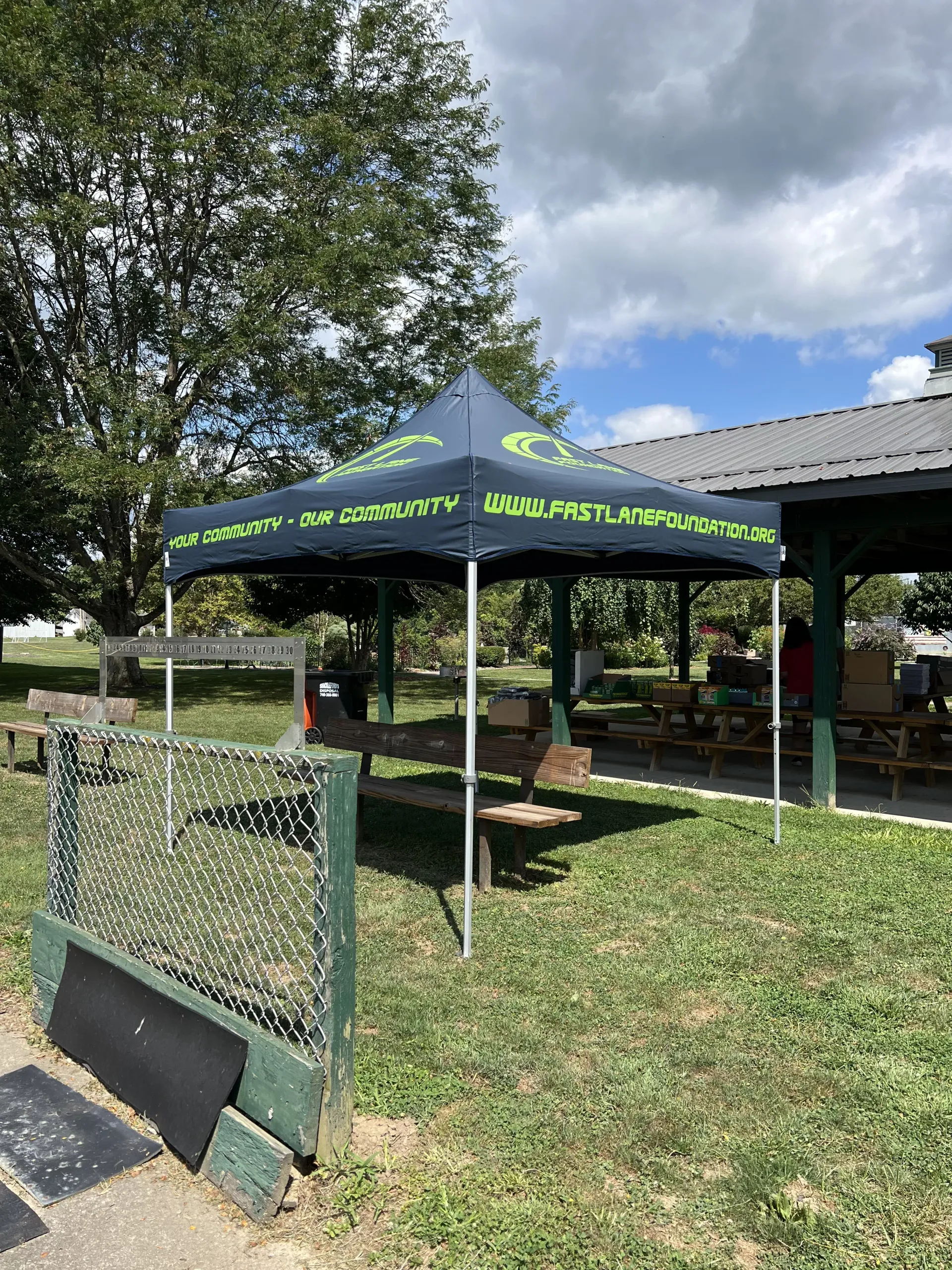 Outdoor tent with green lettering beside a fenced grassy yard under a cloudy sky