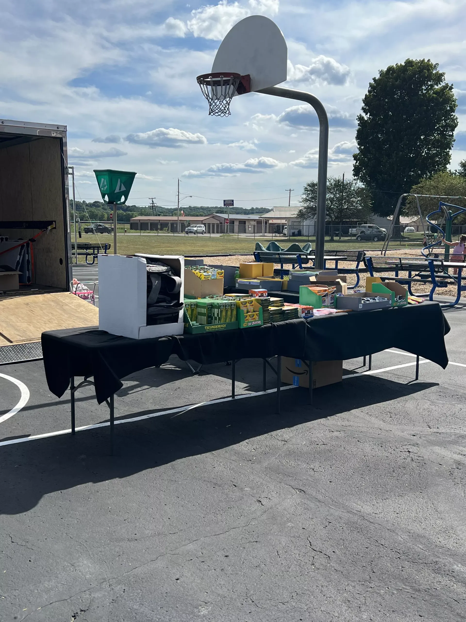 Outdoor table with boxed items and snacks beside a basketball hoop on a court under a sunny sky