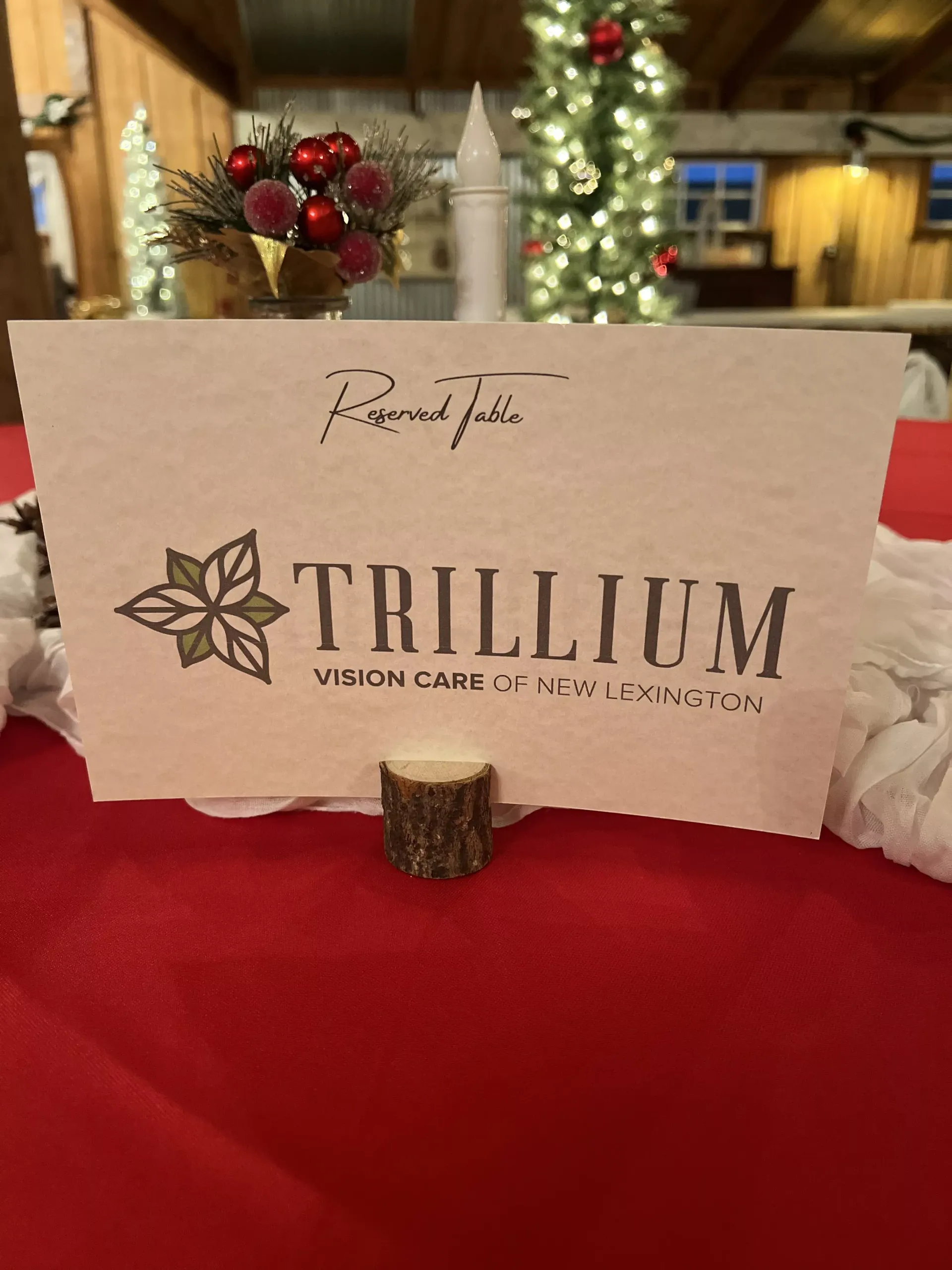 Trillium Vineyards sign on a red tablecloth with festive berries and blurred holiday décor behind it