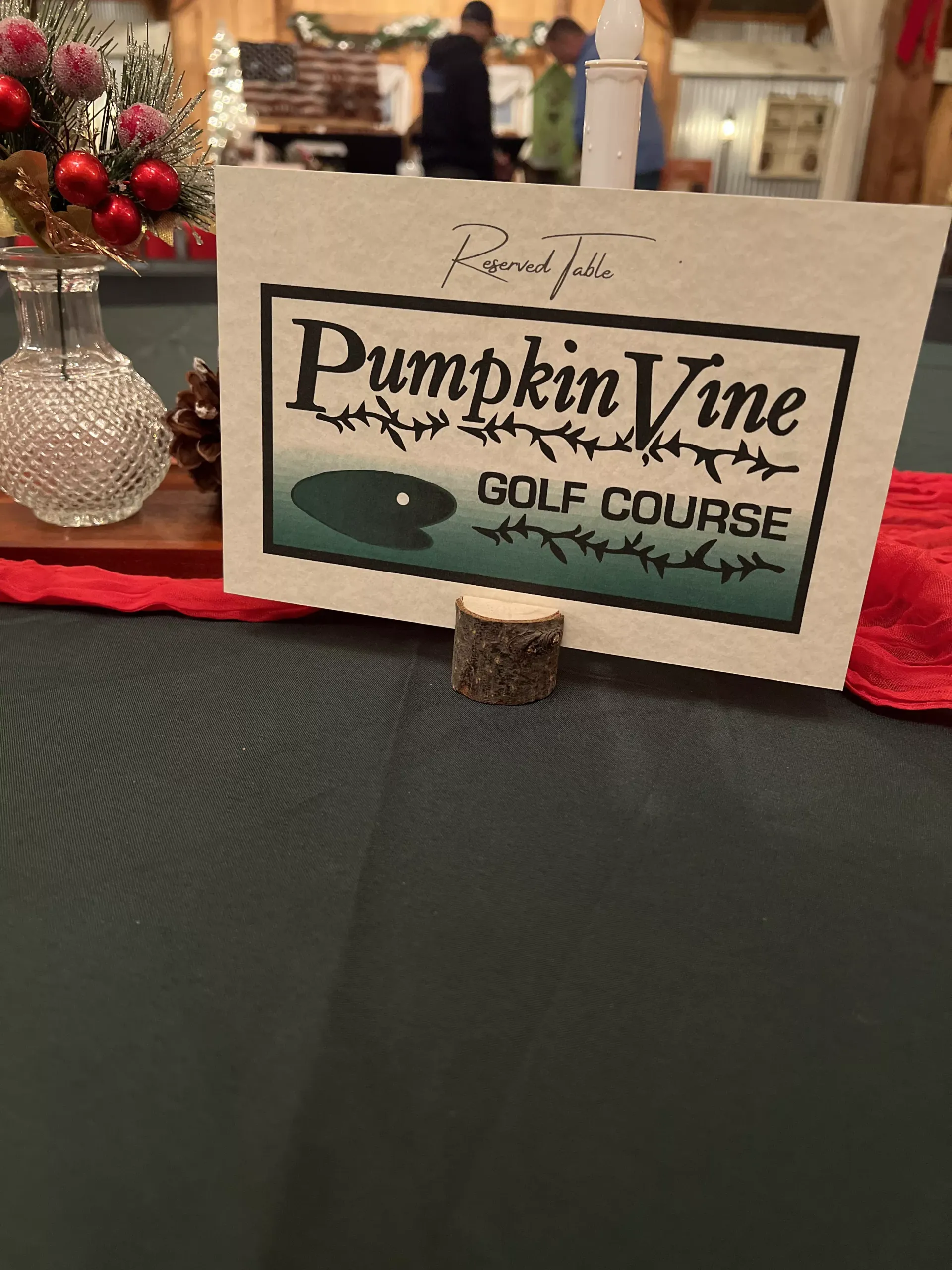 Pumpkin Vine Golf Course sign on a table with red flowers and a patterned tablecloth.