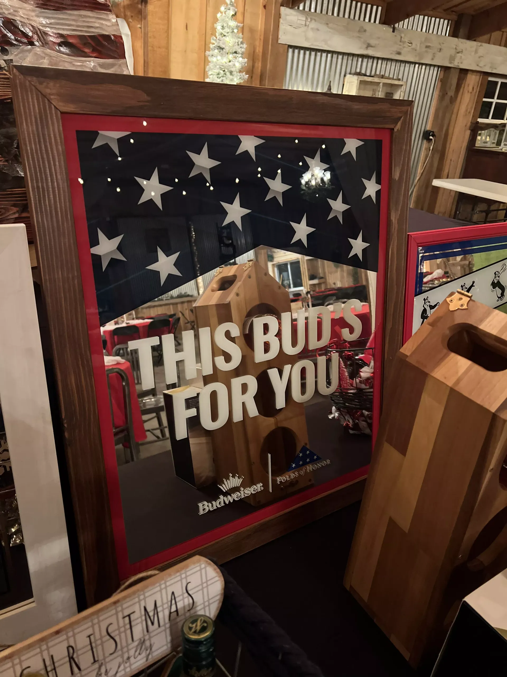 Framed patriotic sign with stars and stripes reading “THIS BUDS FOR YOU” in a rustic shop.