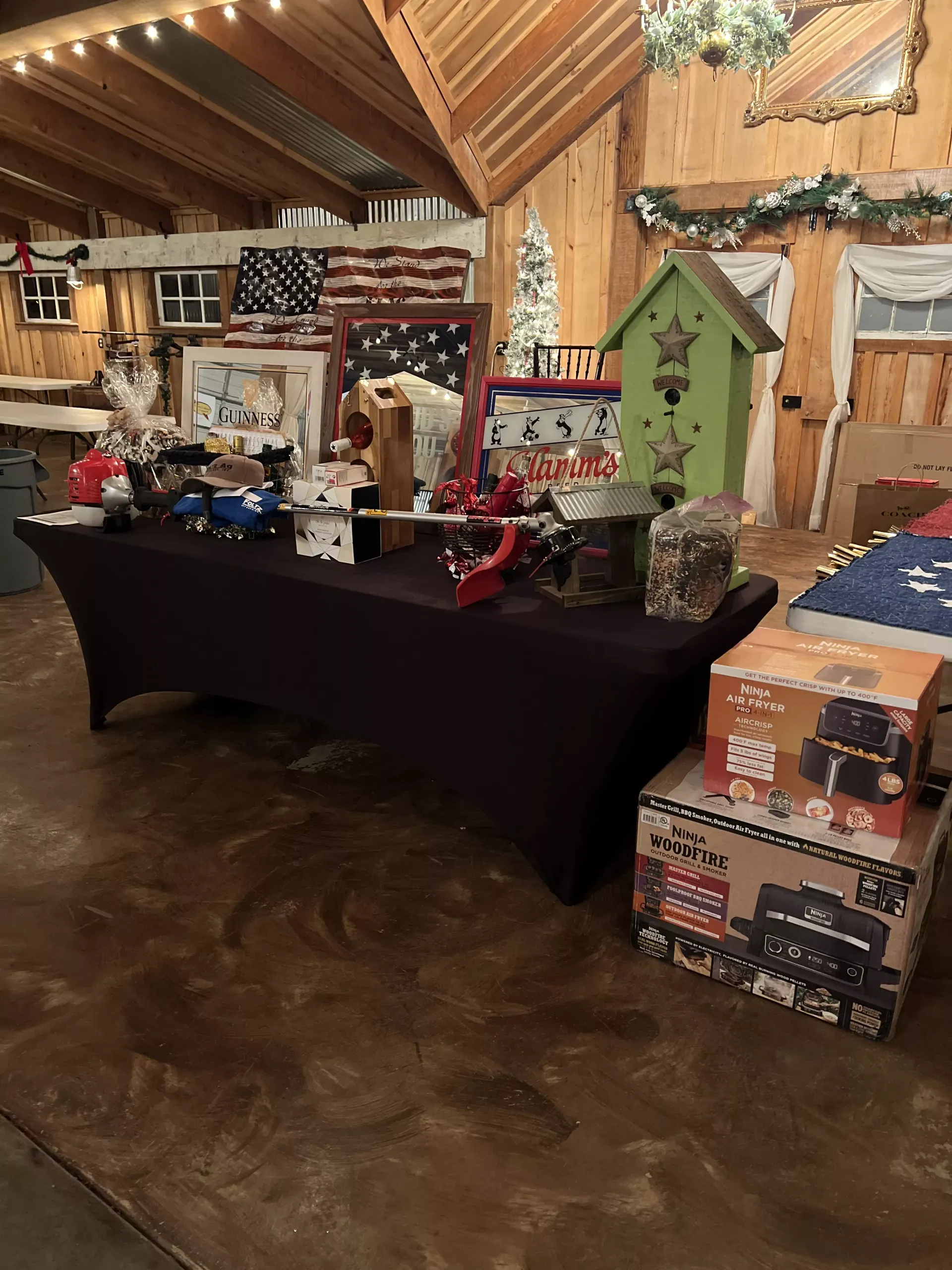 Holiday display table with wrapped gifts, decorations, and signs in a rustic indoor hall