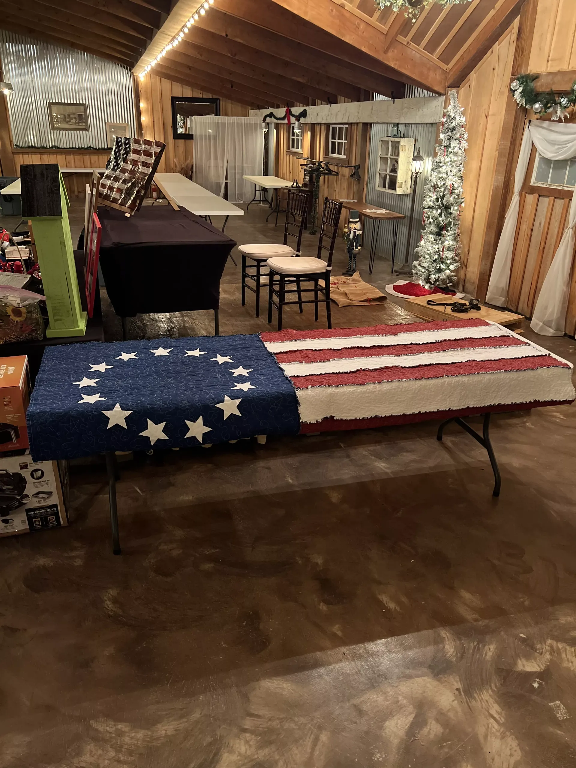 American flag-draped casket in a rustic room with chairs and tables, resembling a memorial or funeral setup