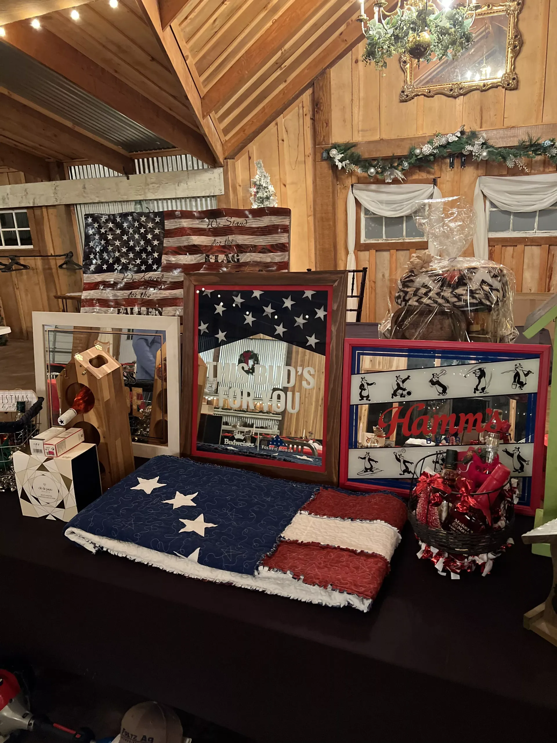 Patriotic memorial display with framed tributes, flags, and red flowers on a table in a rustic room