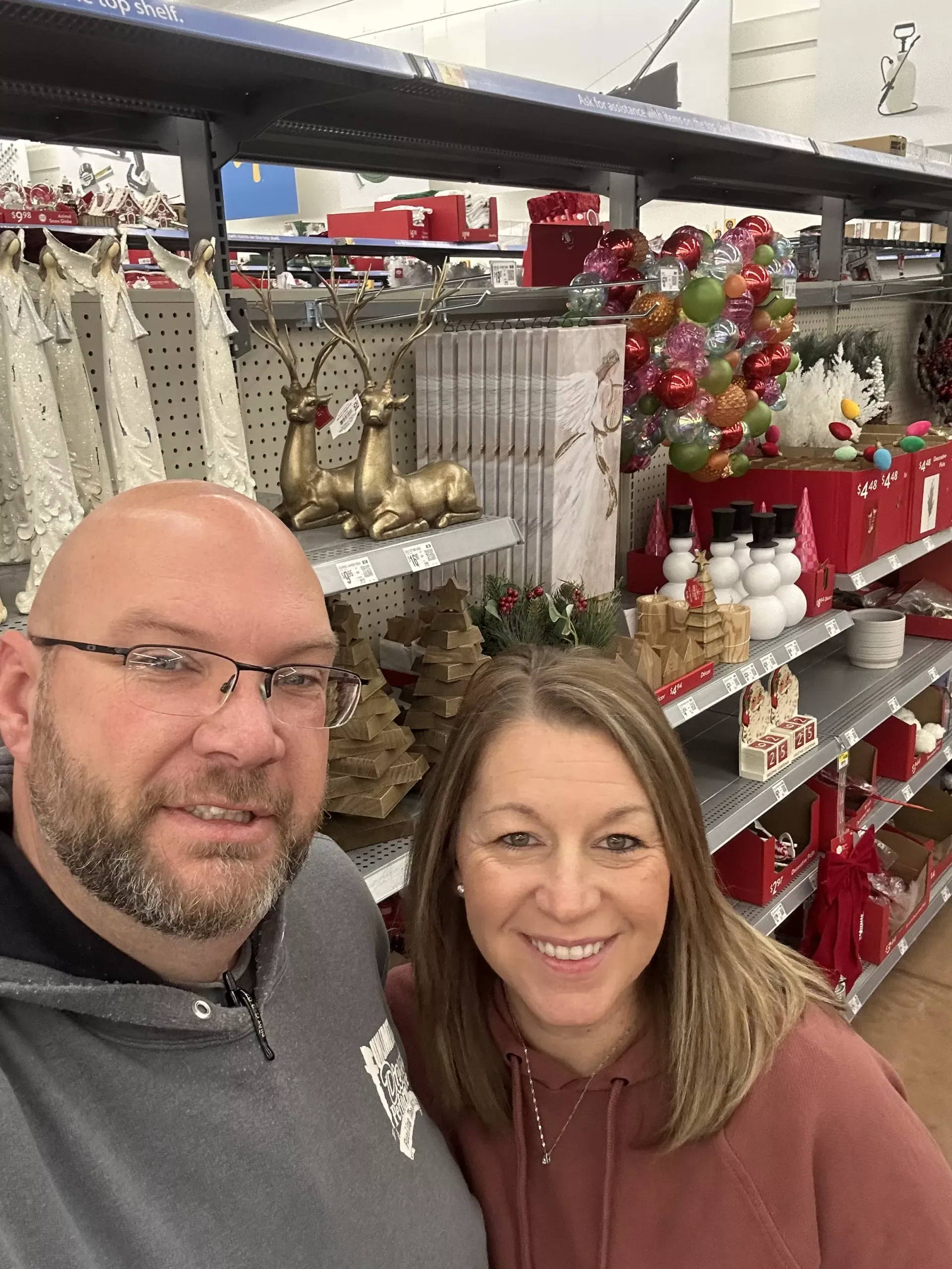Two people smiling in a decorated store aisle with holiday ornaments and shelves behind them