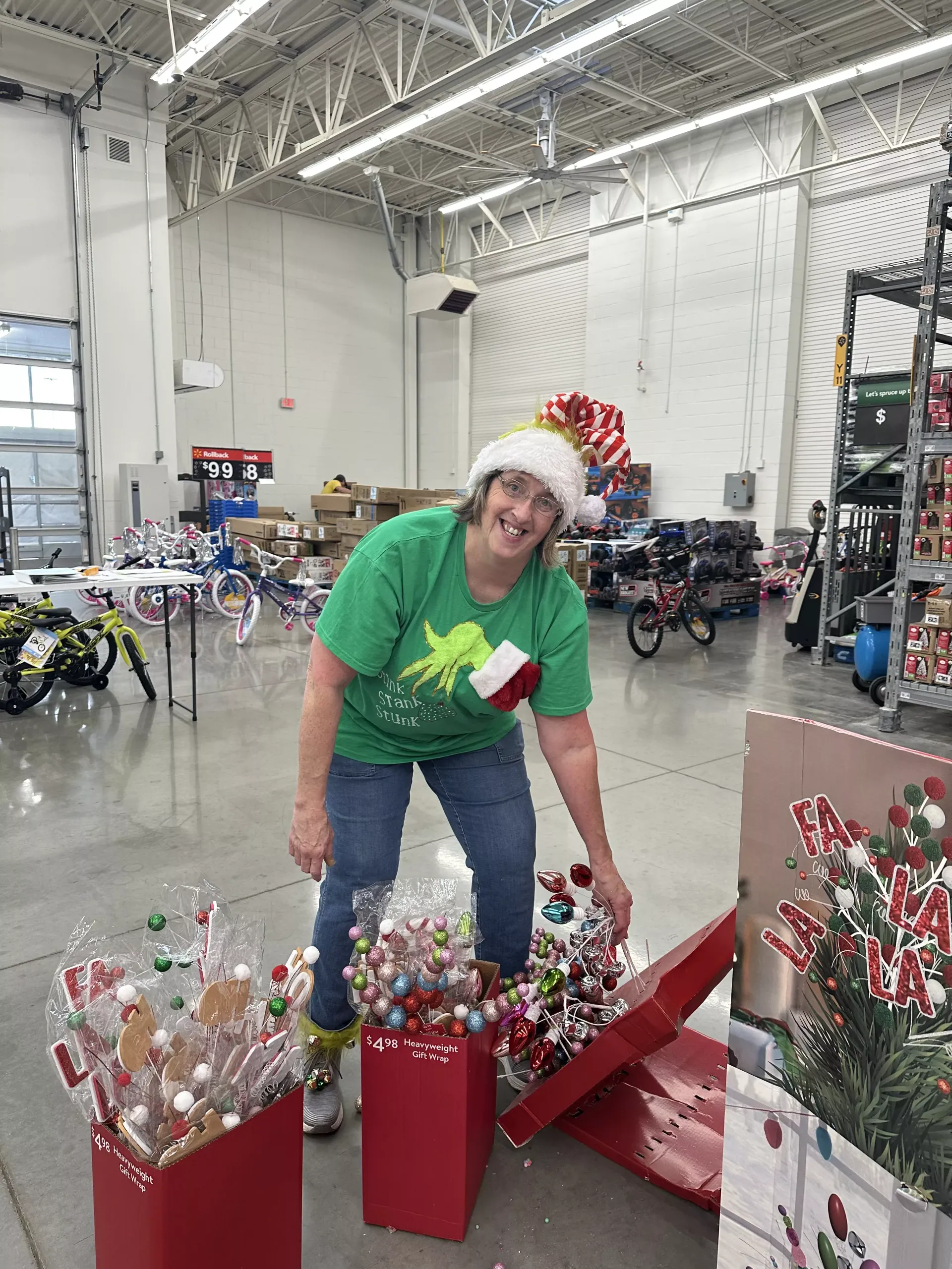 Person in green shirt arranging festive decorations in a warehouse aisle among storage shelves.
