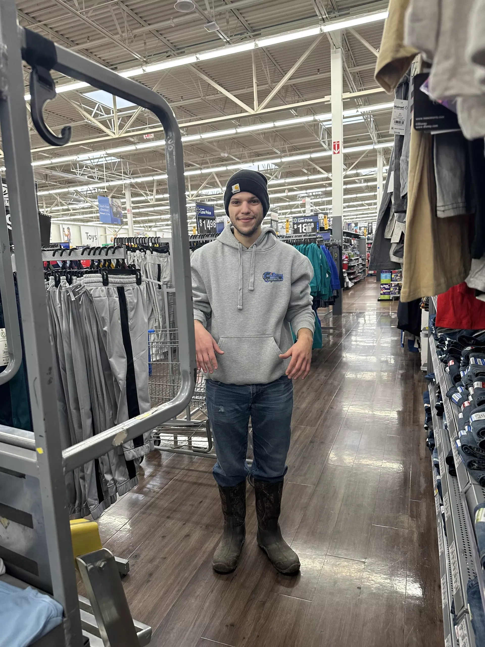 Person standing in a store aisle, wearing a gray hoodie, jeans, beanie, and boots.