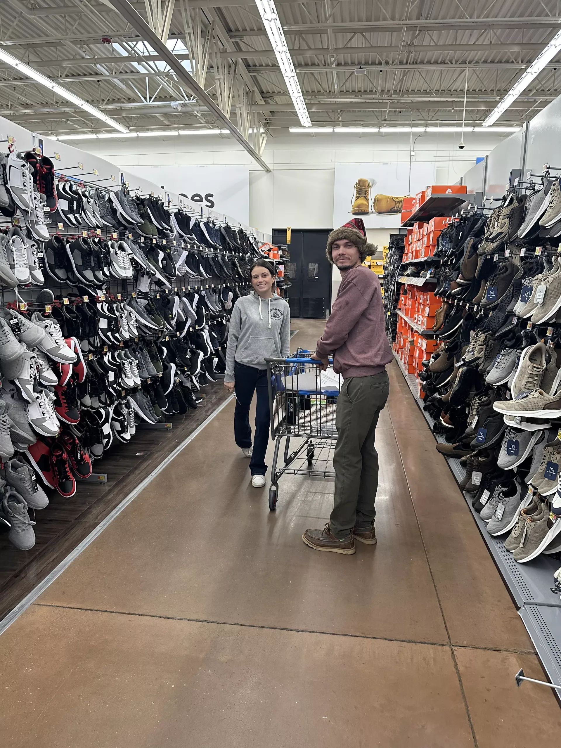 Two shoppers with a cart in a store aisle lined with shoes