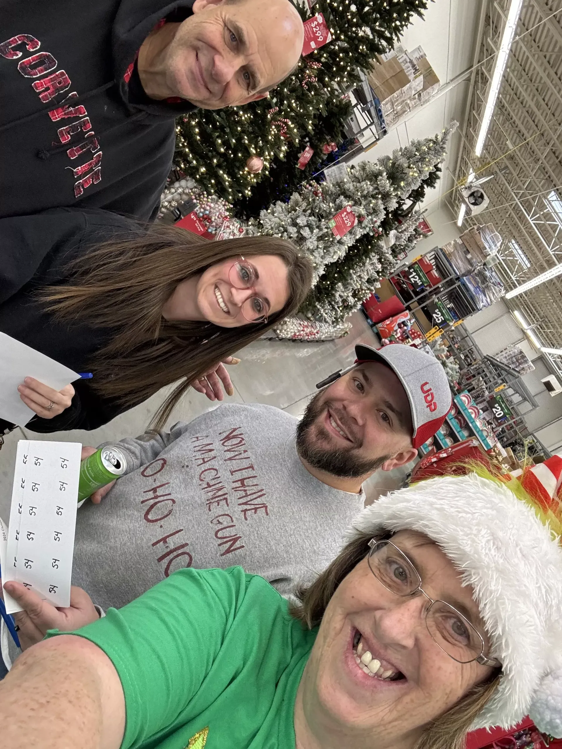 Four people smiling for a selfie in a holiday store aisle with decorated Christmas trees.