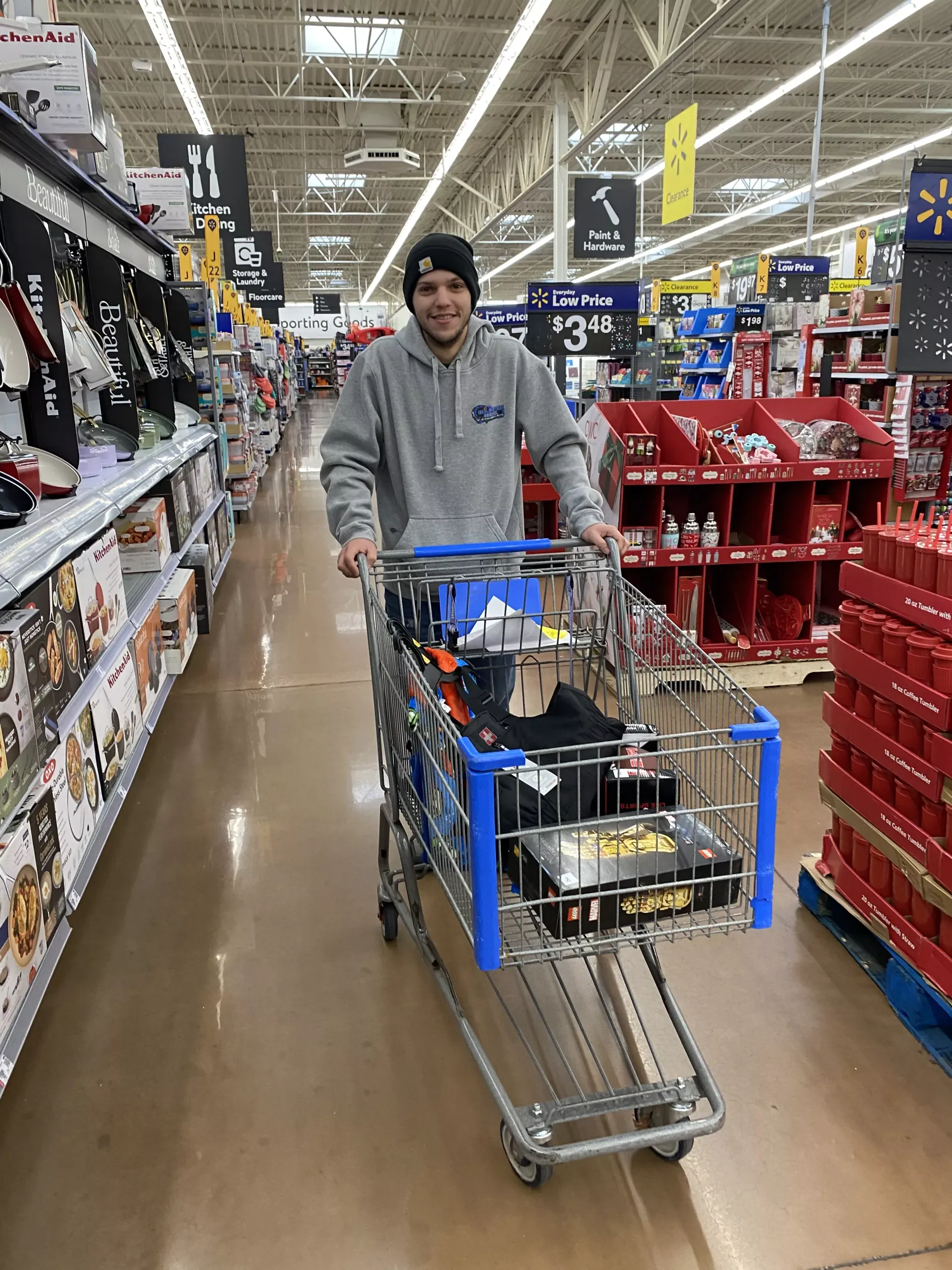 Shopper in gray hoodie pushes a cart through a brightly lit store aisle.