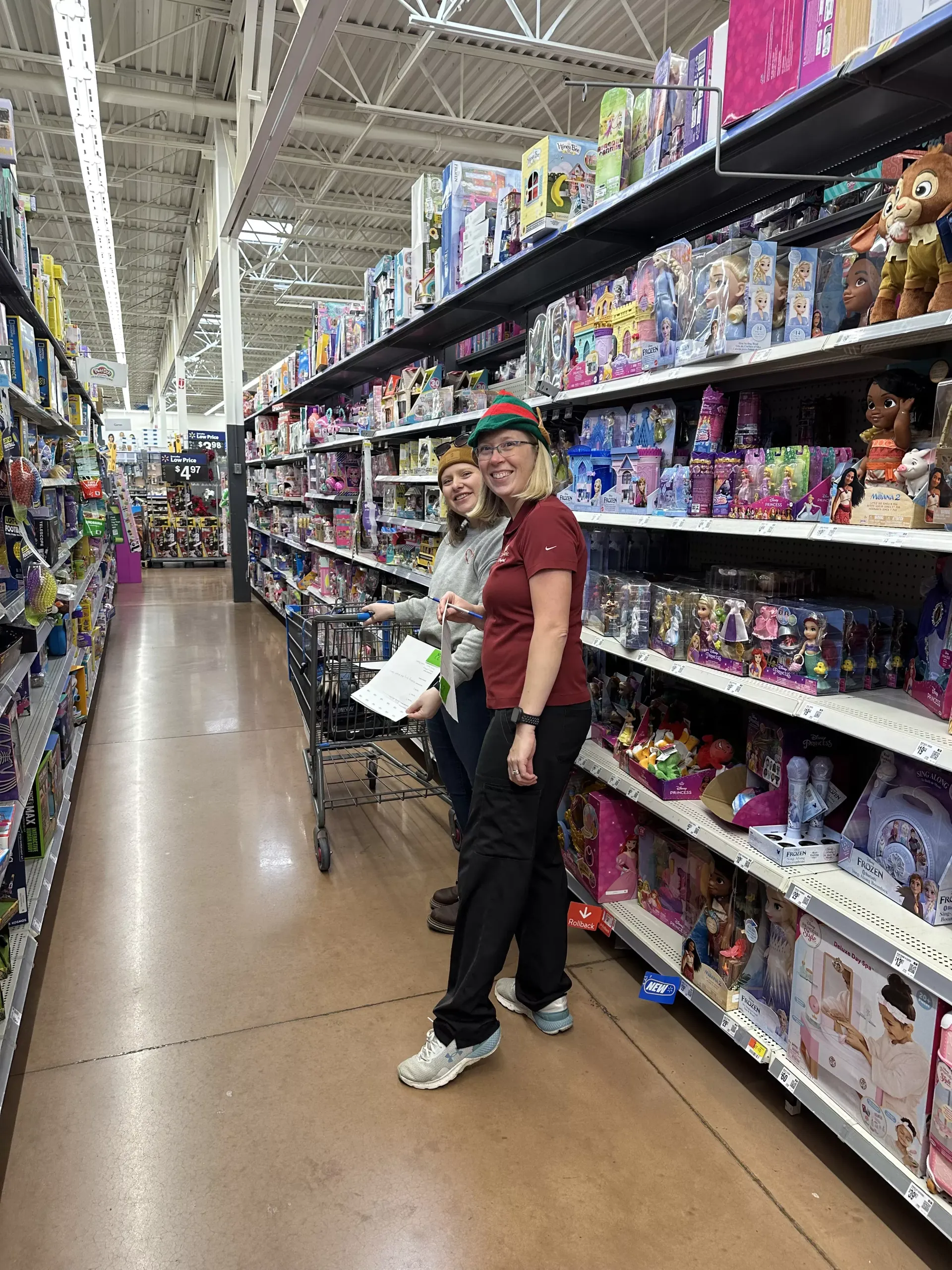 Person standing in a toy store aisle, holding a box and smiling at the camera.