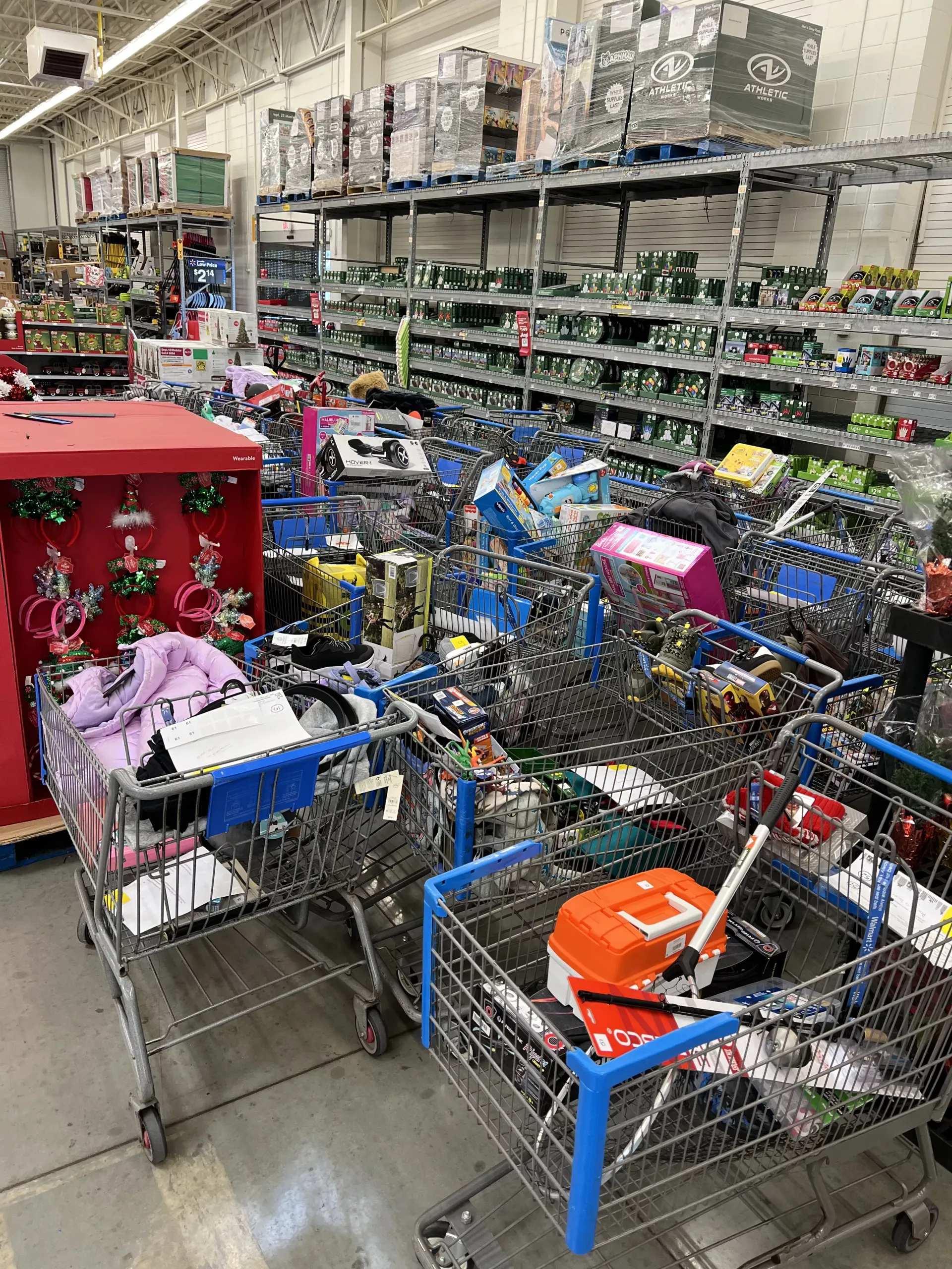 Shopping carts piled high with toy boxes and items in a store aisle, with shelves of stock in the background.