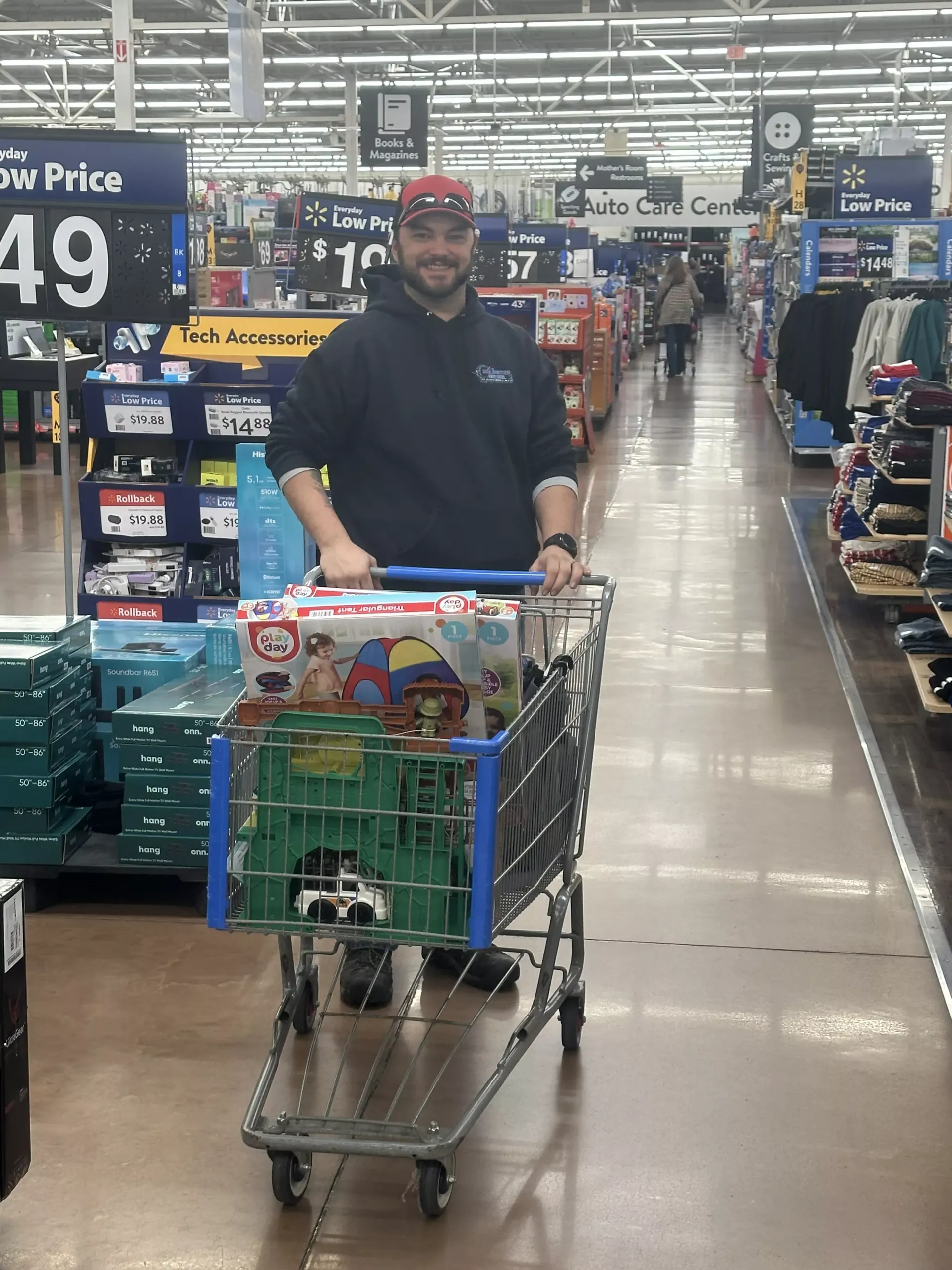 Man shopping in a Walmart aisle, pushing a cart loaded with toy boxes.