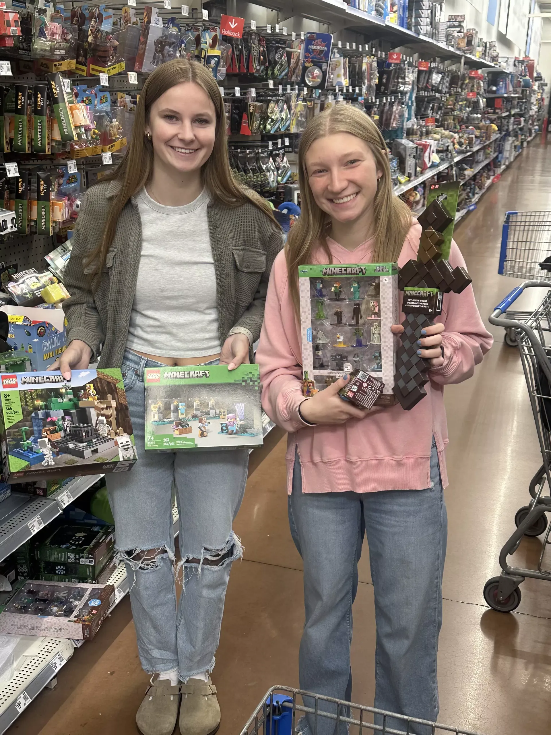 Two women holding toy boxes in a store aisle, smiling at the camera.