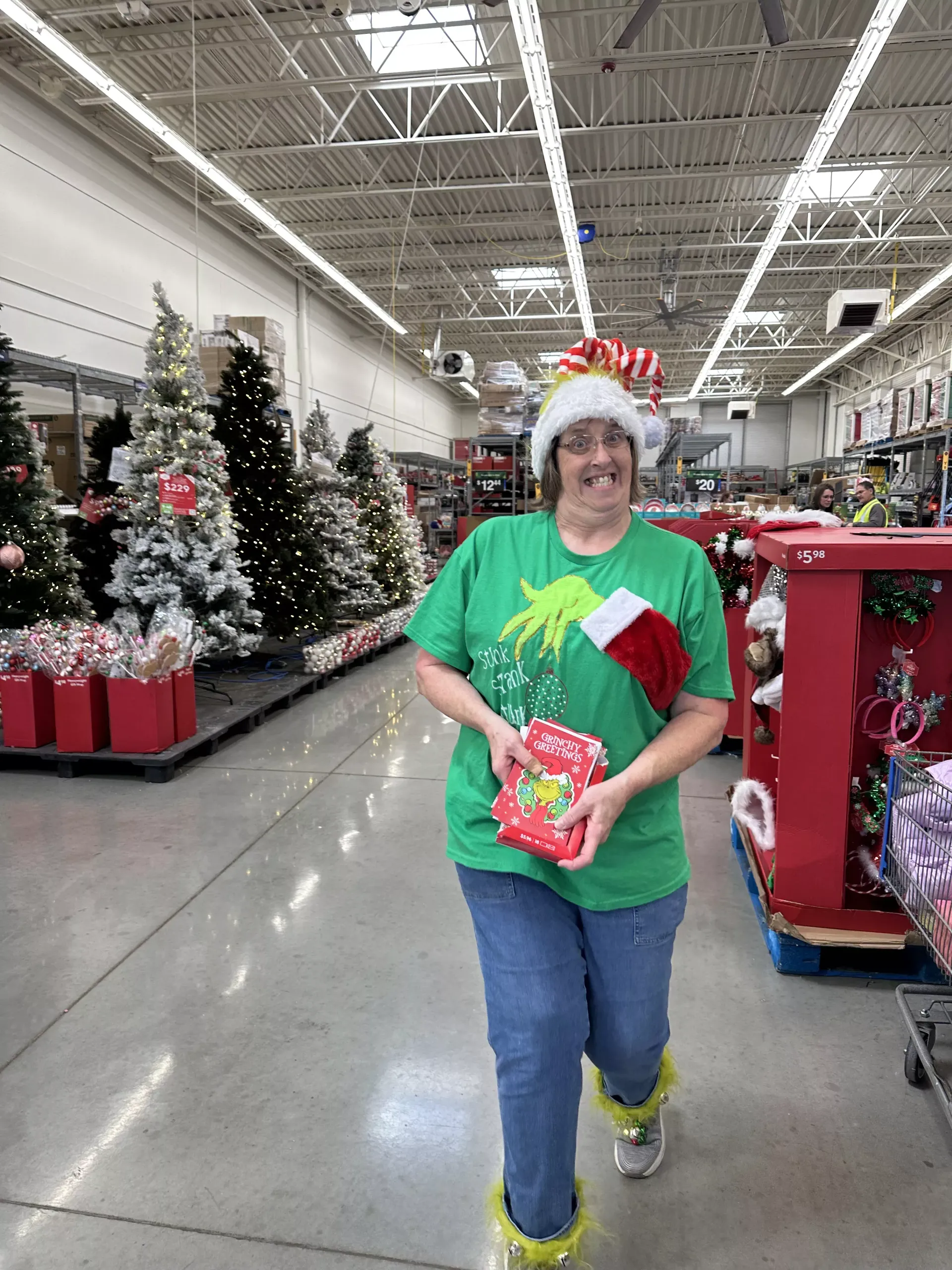 Person in a Christmas aisle holding a wrapped gift, with decorated trees and holiday displays behind.