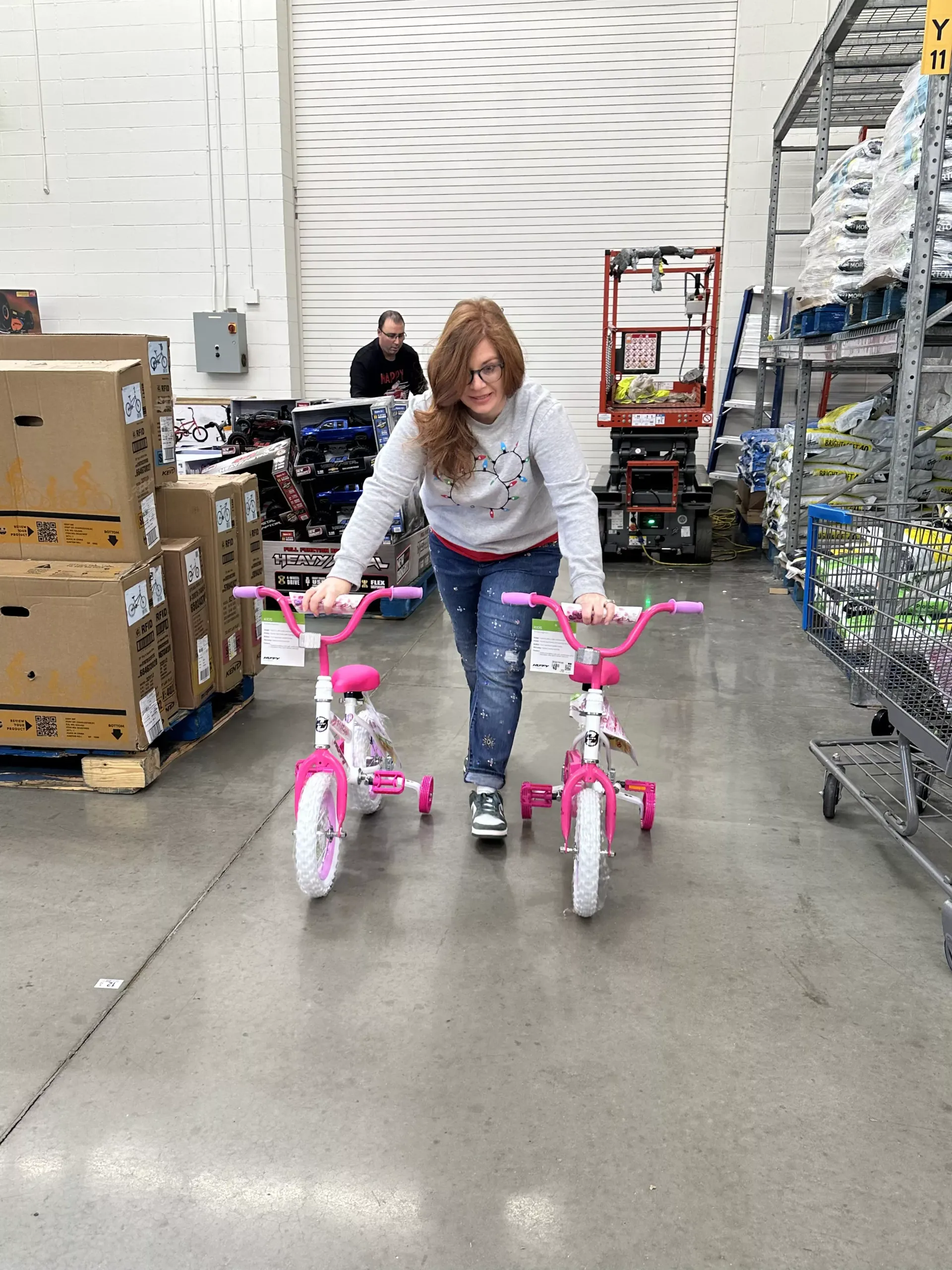 Woman pushing two pink children's bicycles in a warehouse aisle