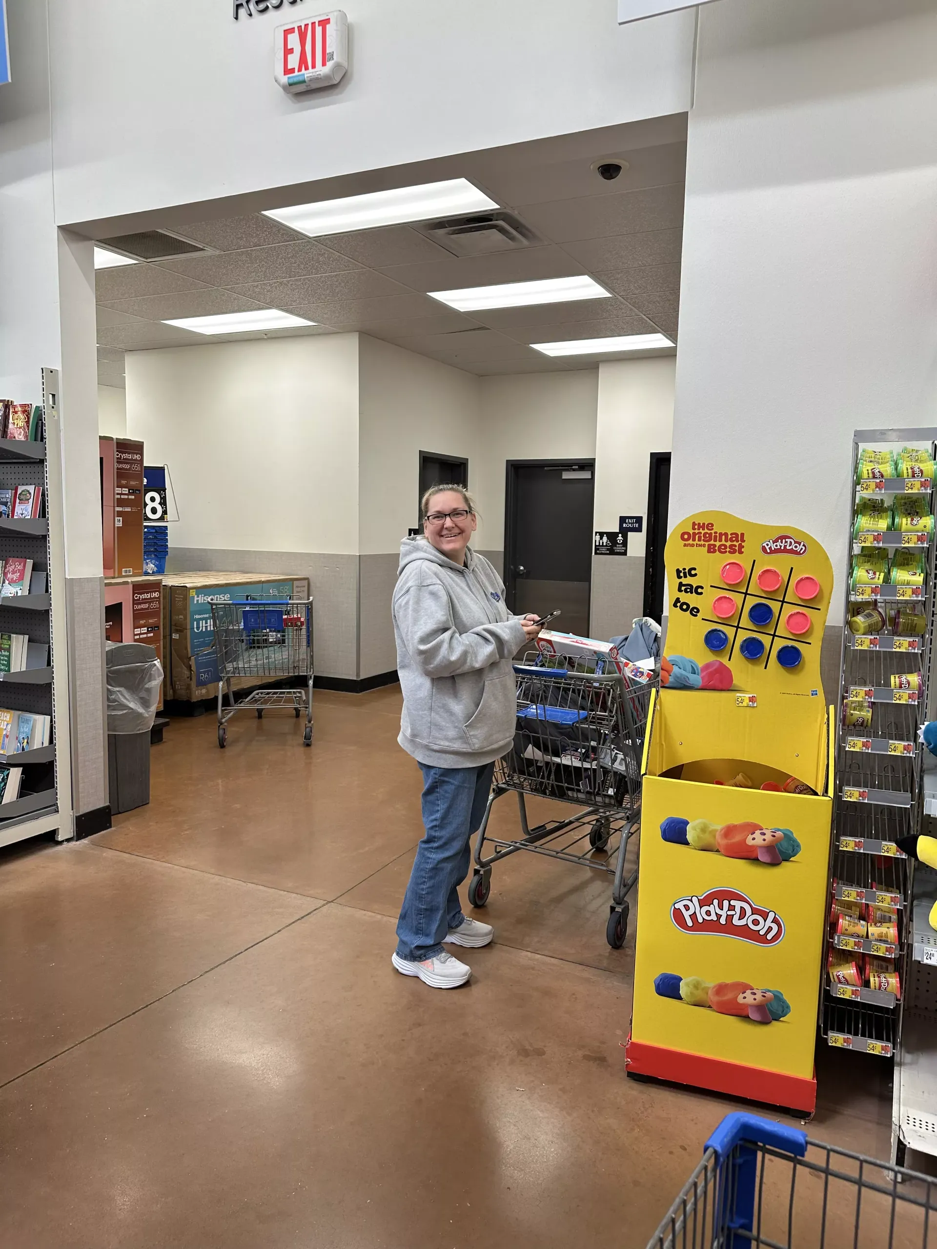 Woman standing by shopping carts in a store aisle near a bright yellow candy display.