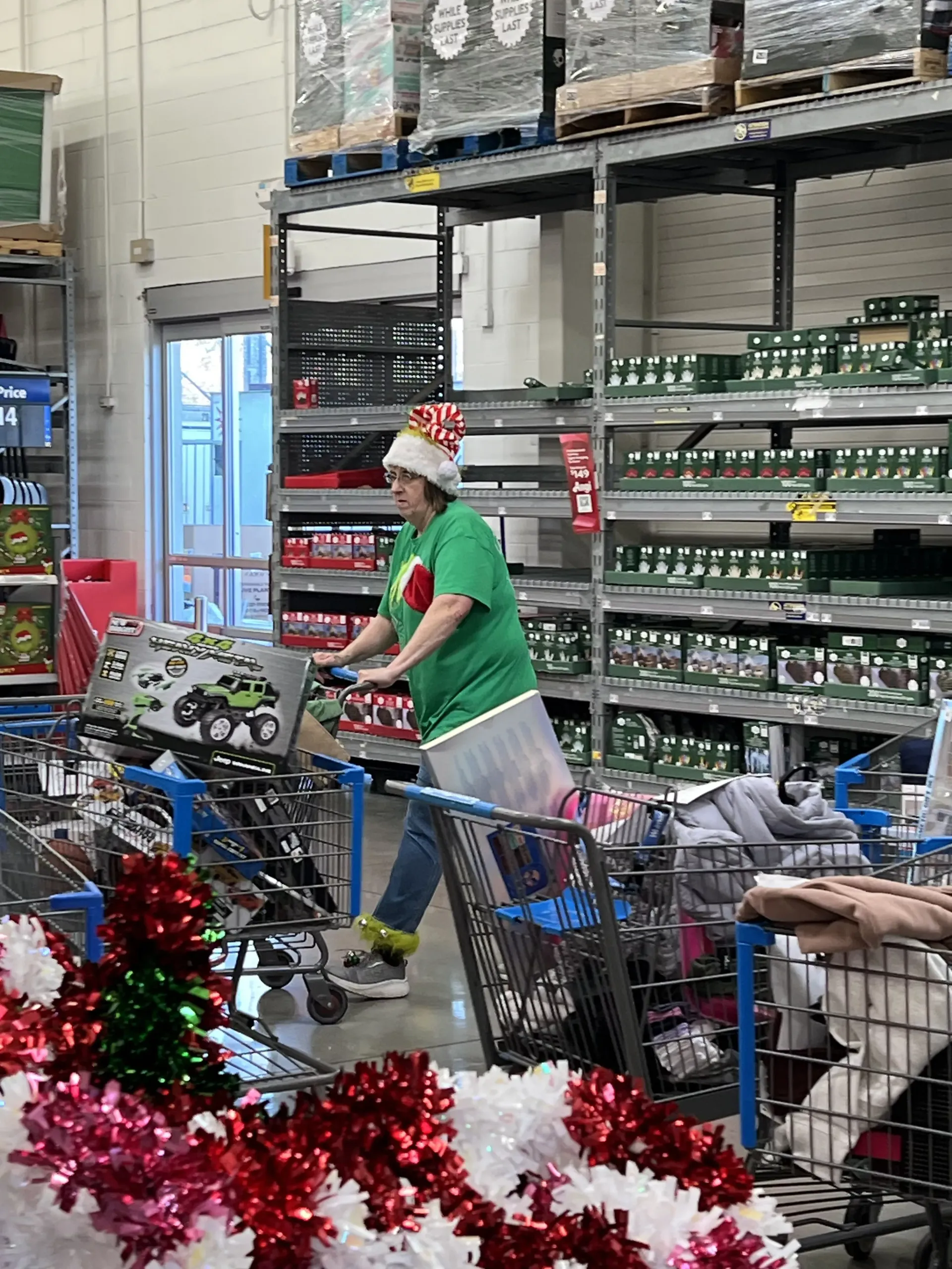 Person in a red Santa hat pushing a cart in a store aisle with holiday decorations in the foreground