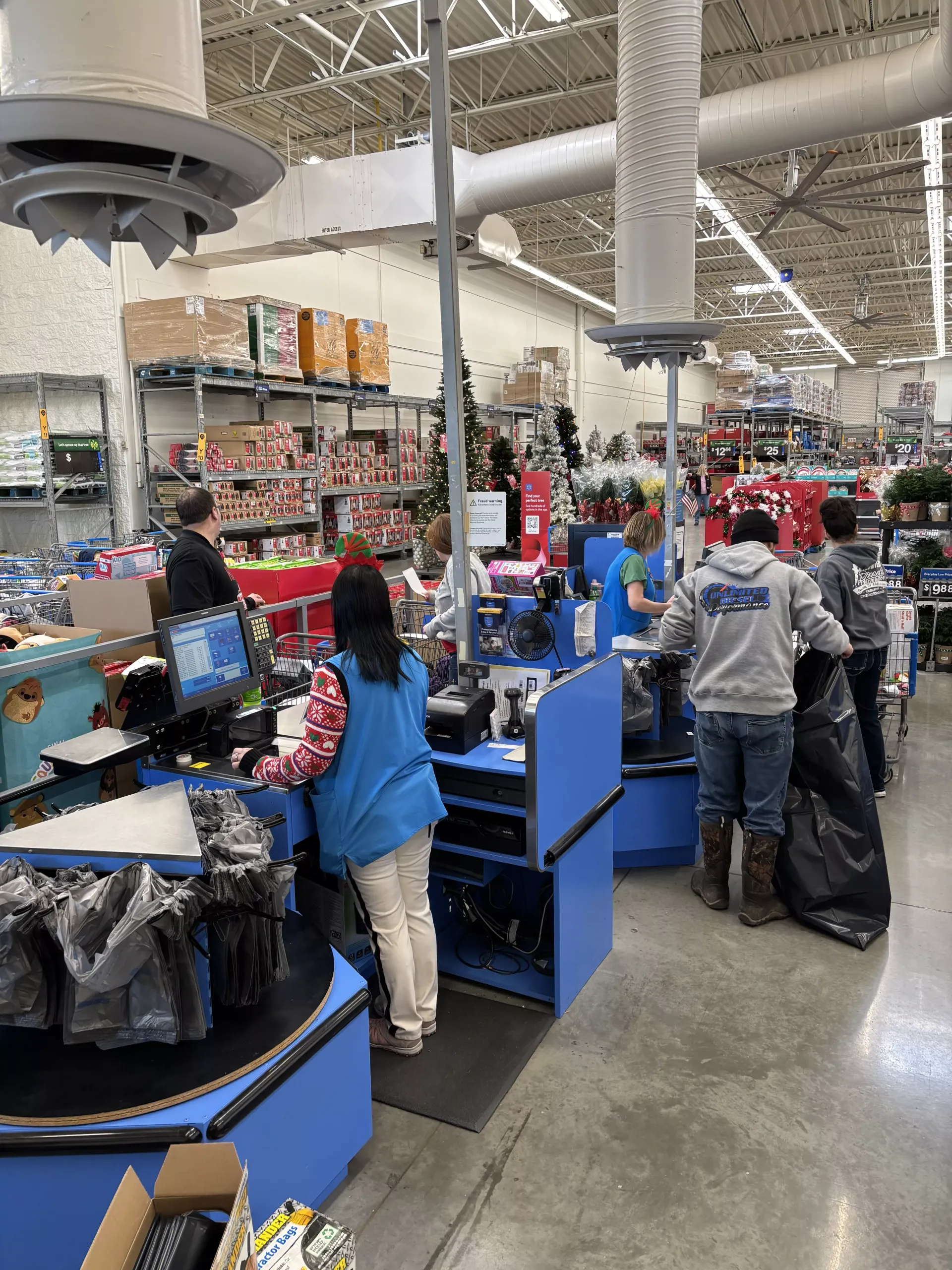 Shoppers at Walmart self-checkout counters with blue stations and overhead lights in a busy store.