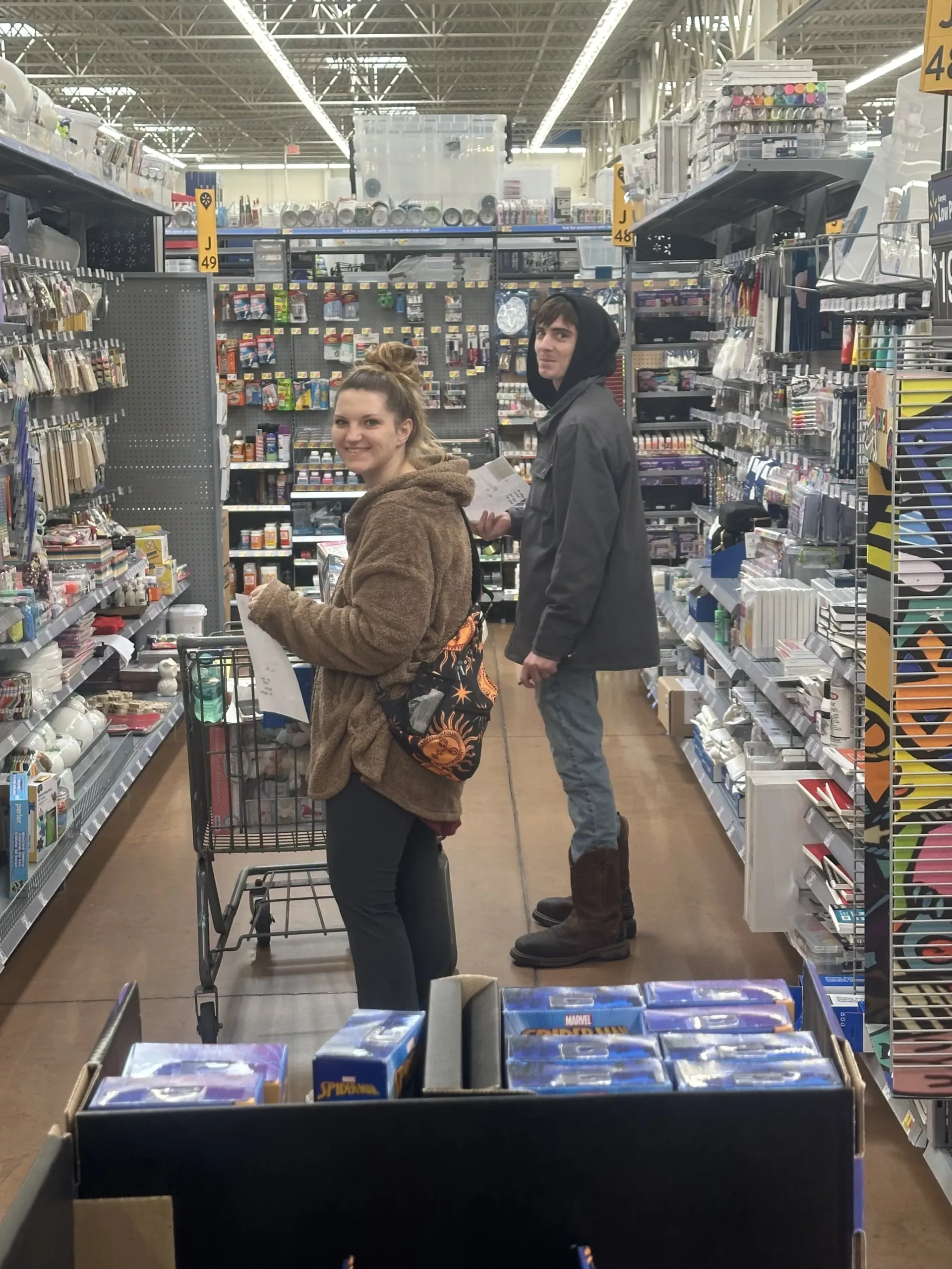 Two shoppers in a brightly lit store aisle, one smiling toward the camera.