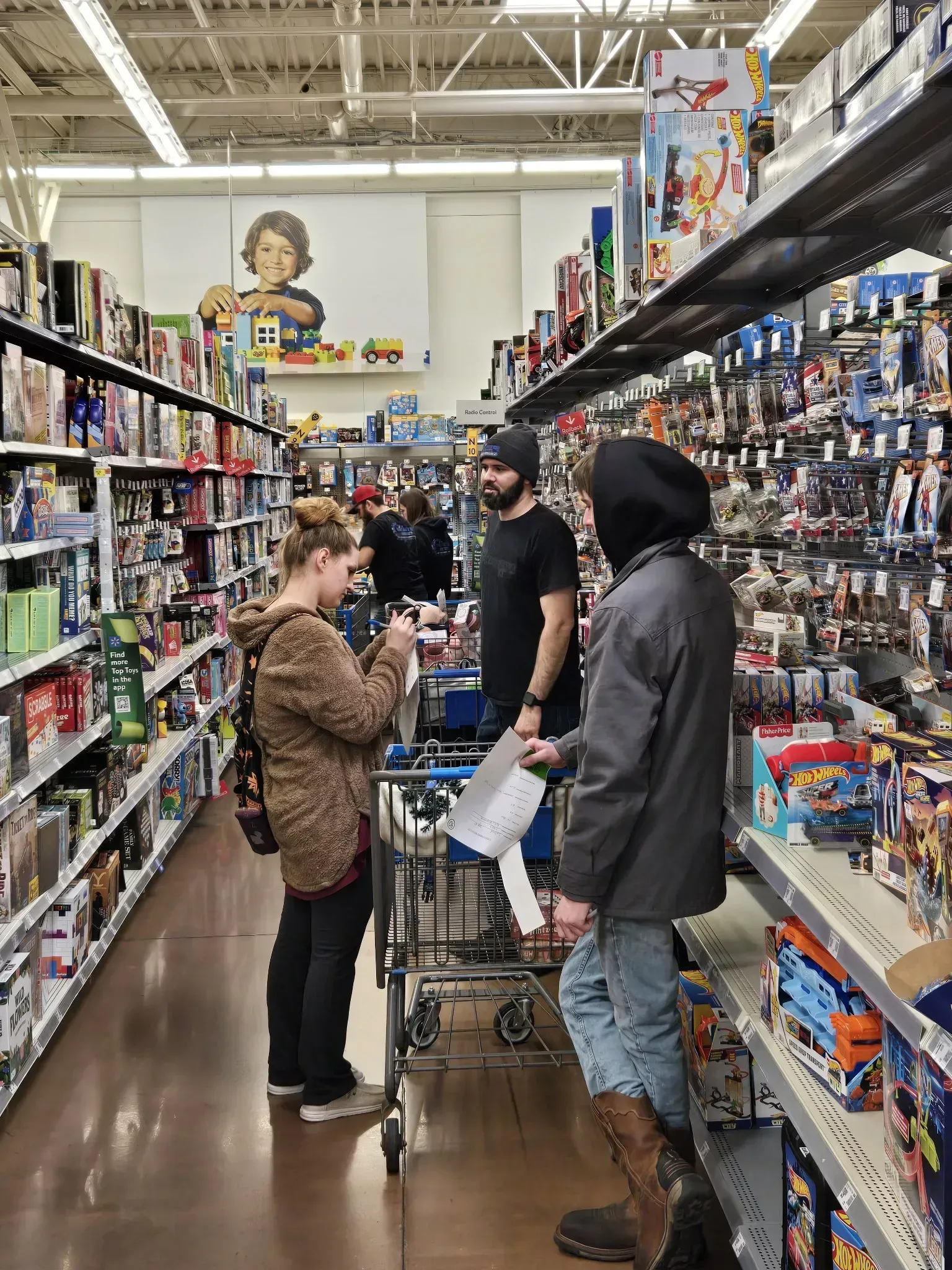 Three people browsing toy aisles in a store, with carts and shelves full of toys.