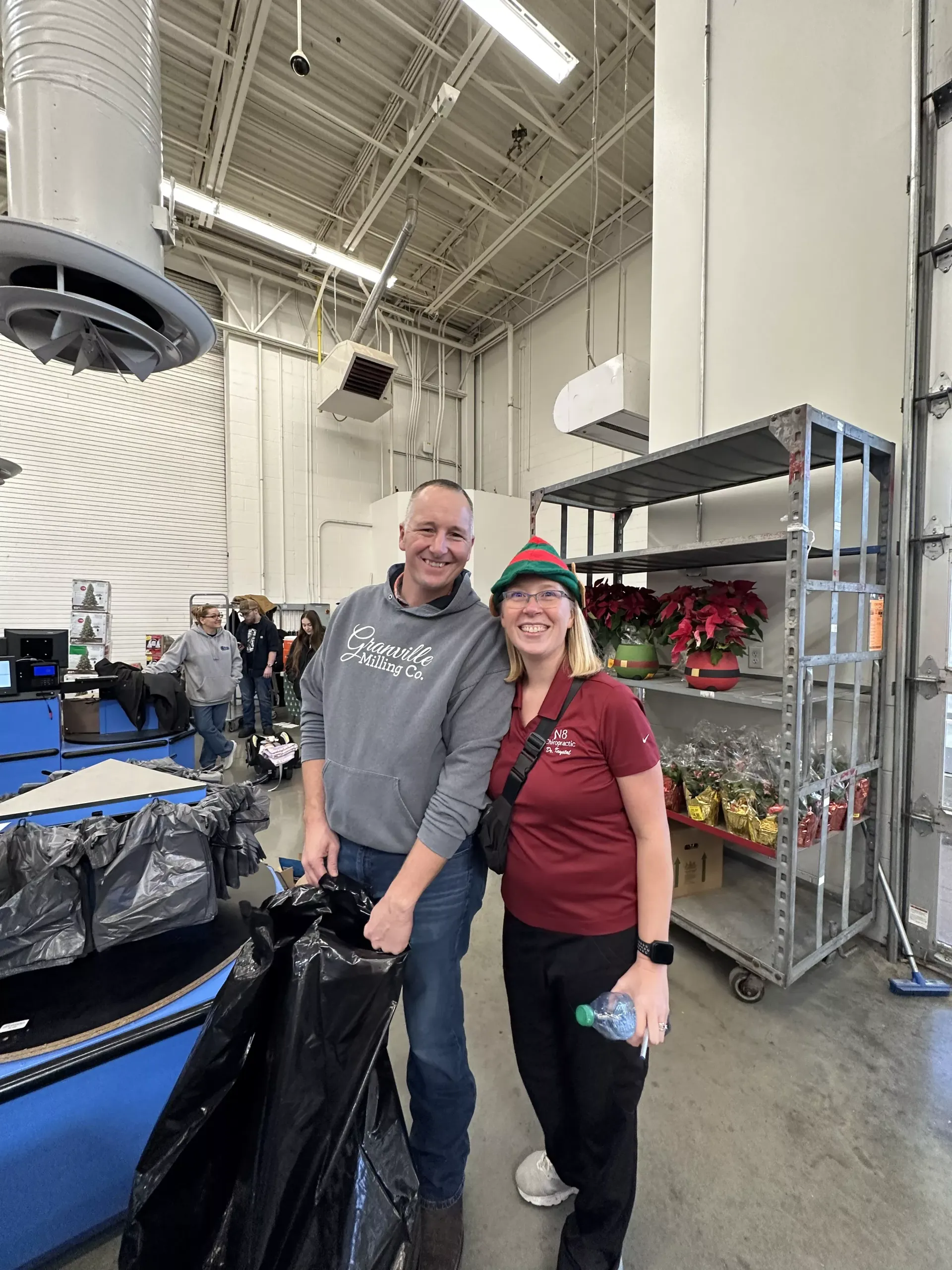 Two smiling people standing in a warehouse aisle beside metal shelving and equipment