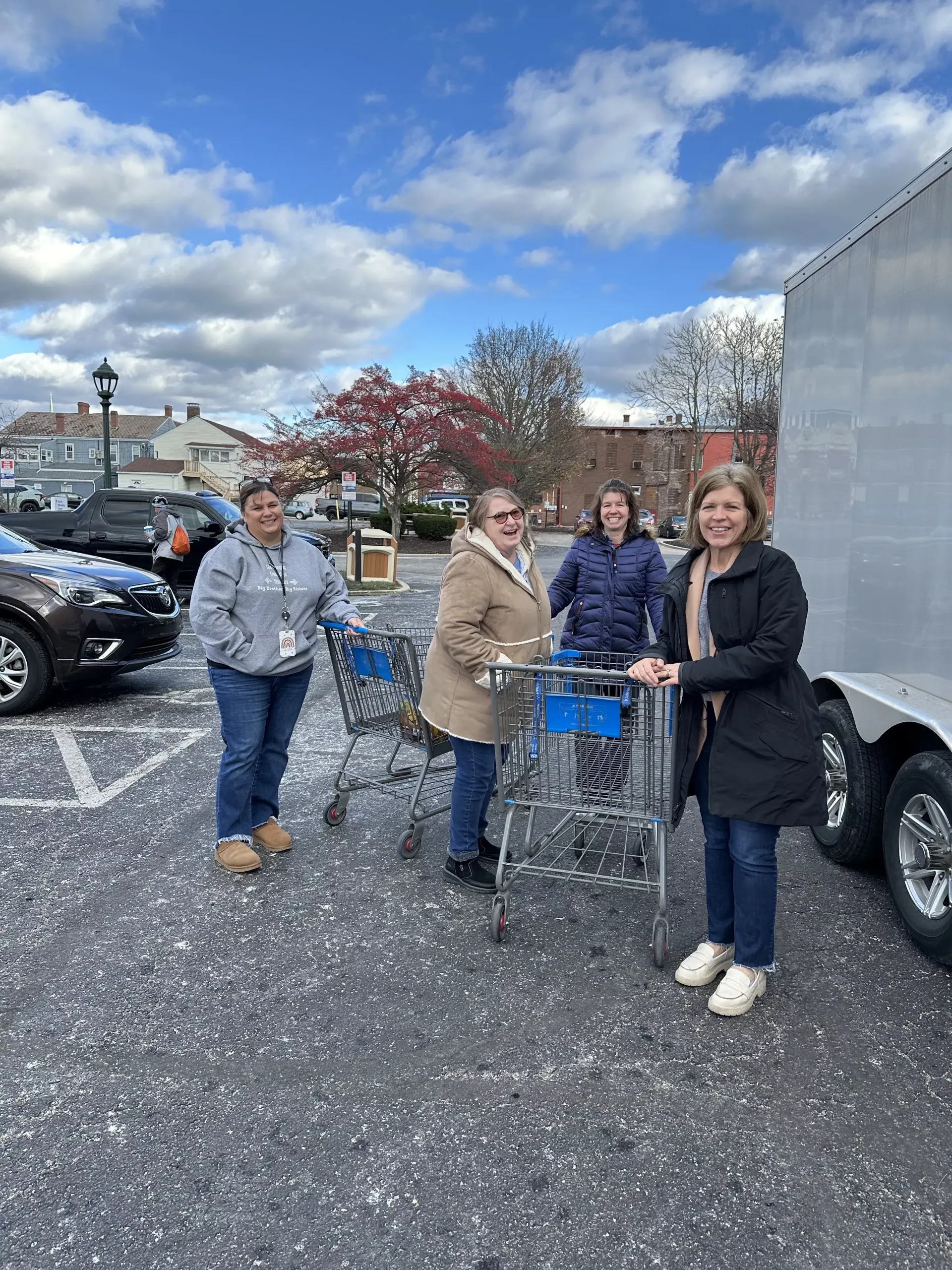Four people stand with shopping carts in a parking lot under a cloudy sky.