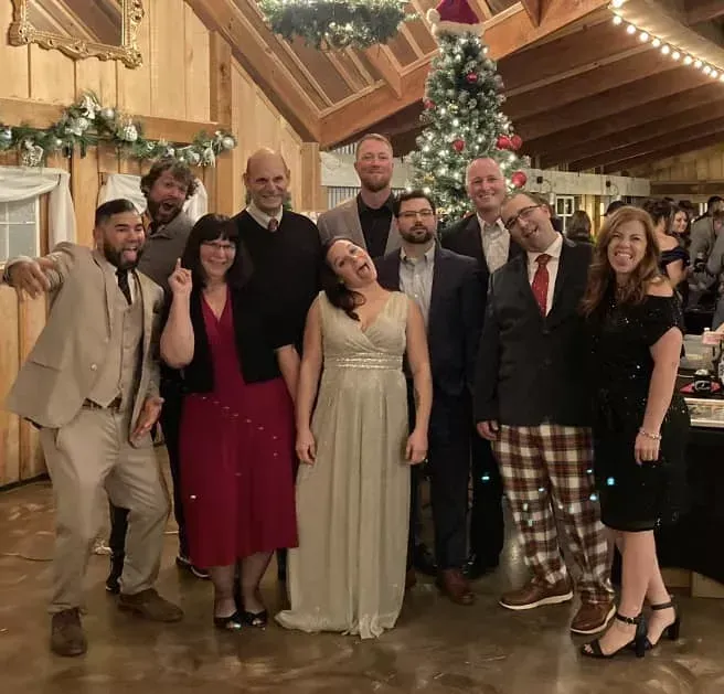 Group of eight people smiling and posing in festive holiday attire in a decorated wooden hall