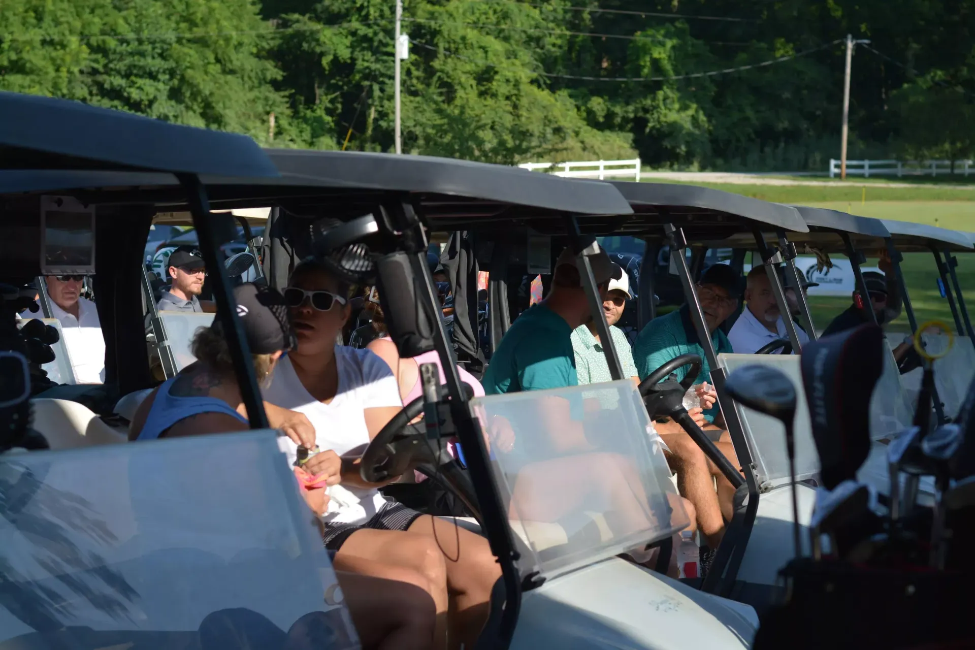 Passengers seated in an open-air golf cart driving along a grassy roadside