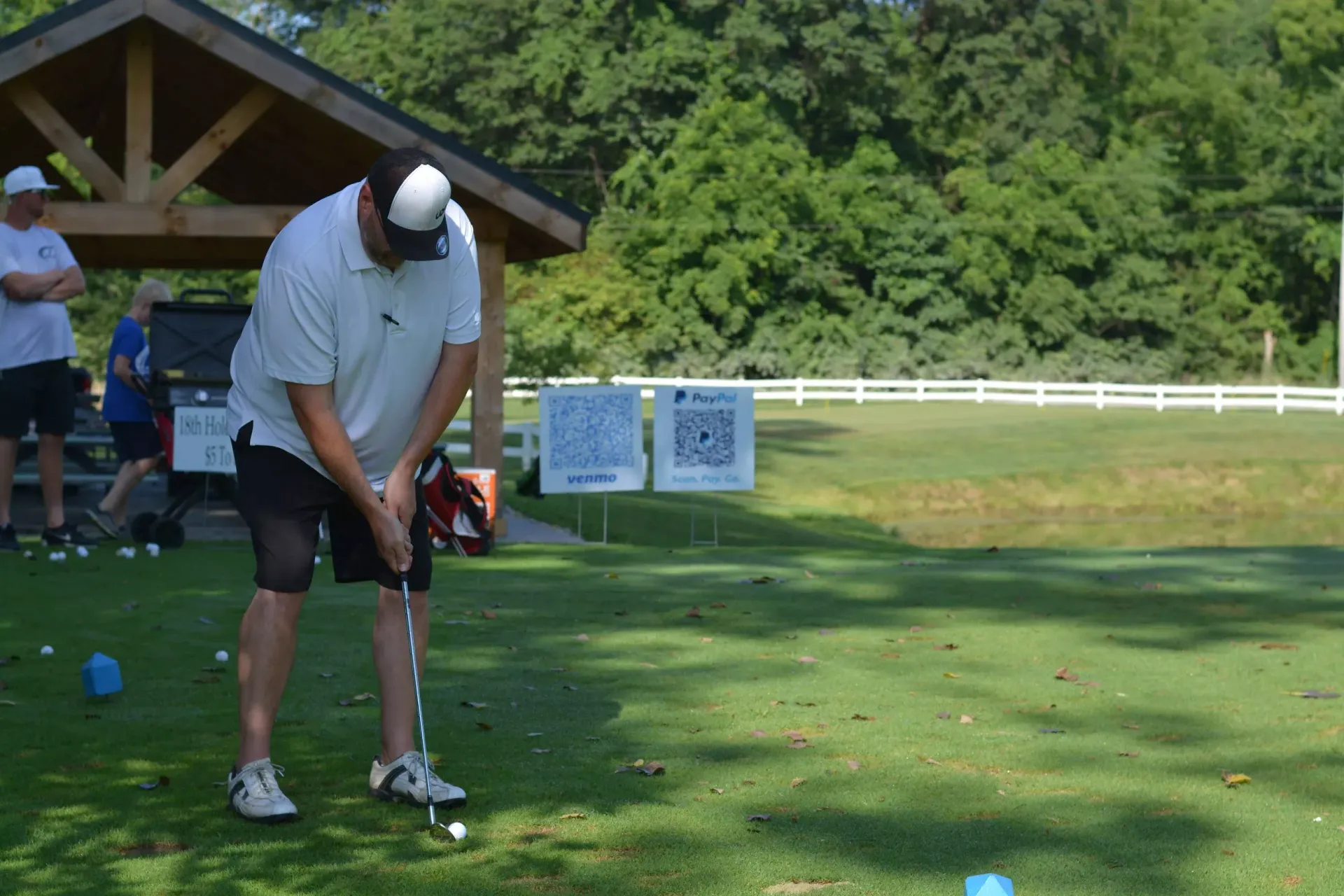 Golfer in white shirt and black shorts putting on a green course near a wooden shelter