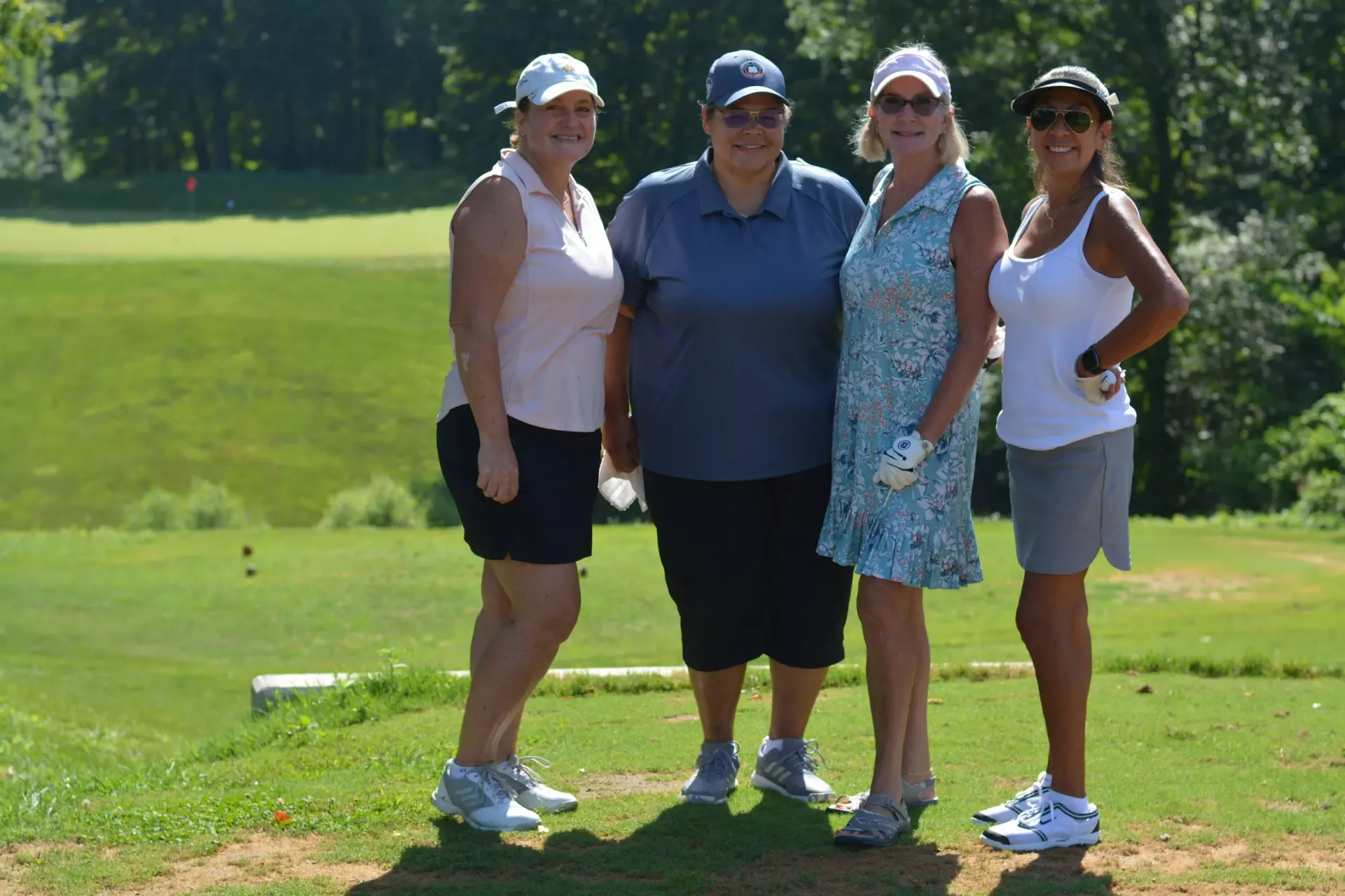 Four people posing together on a sunny golf course, wearing caps and athletic clothing.