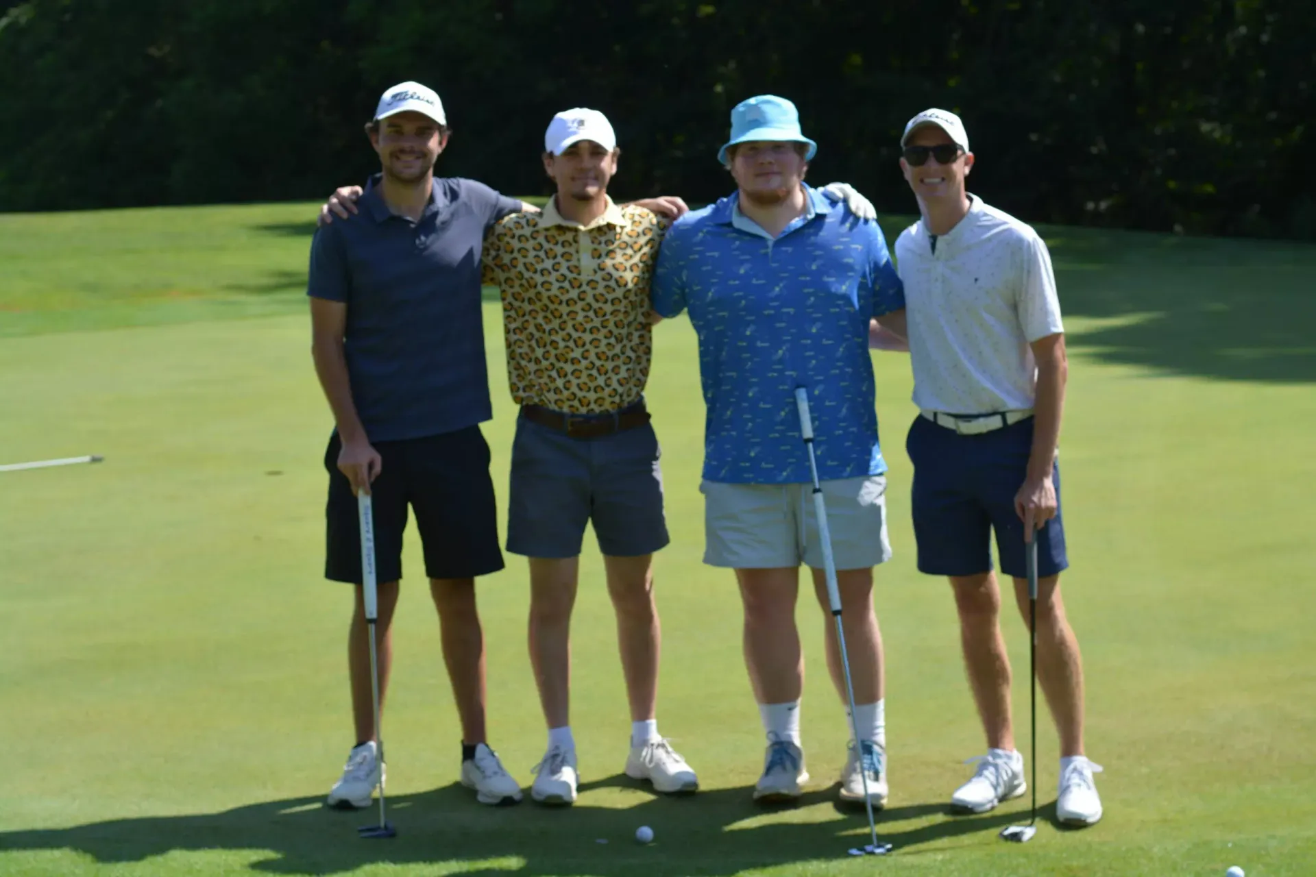 Four golfers standing together on a sunny golf course, holding clubs and posing for a photo