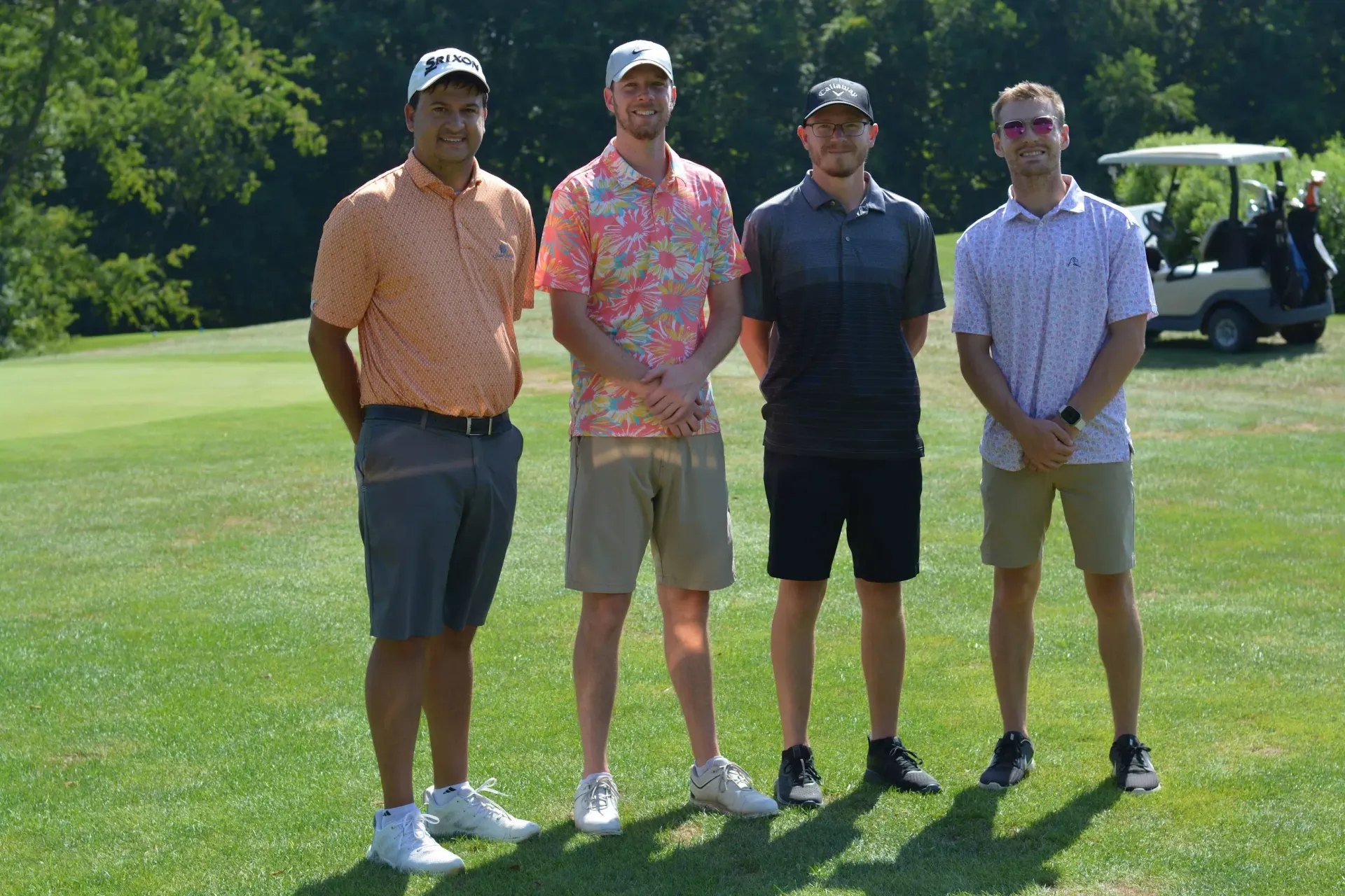 Four golfers standing on a sunny green fairway with a golf cart in the background