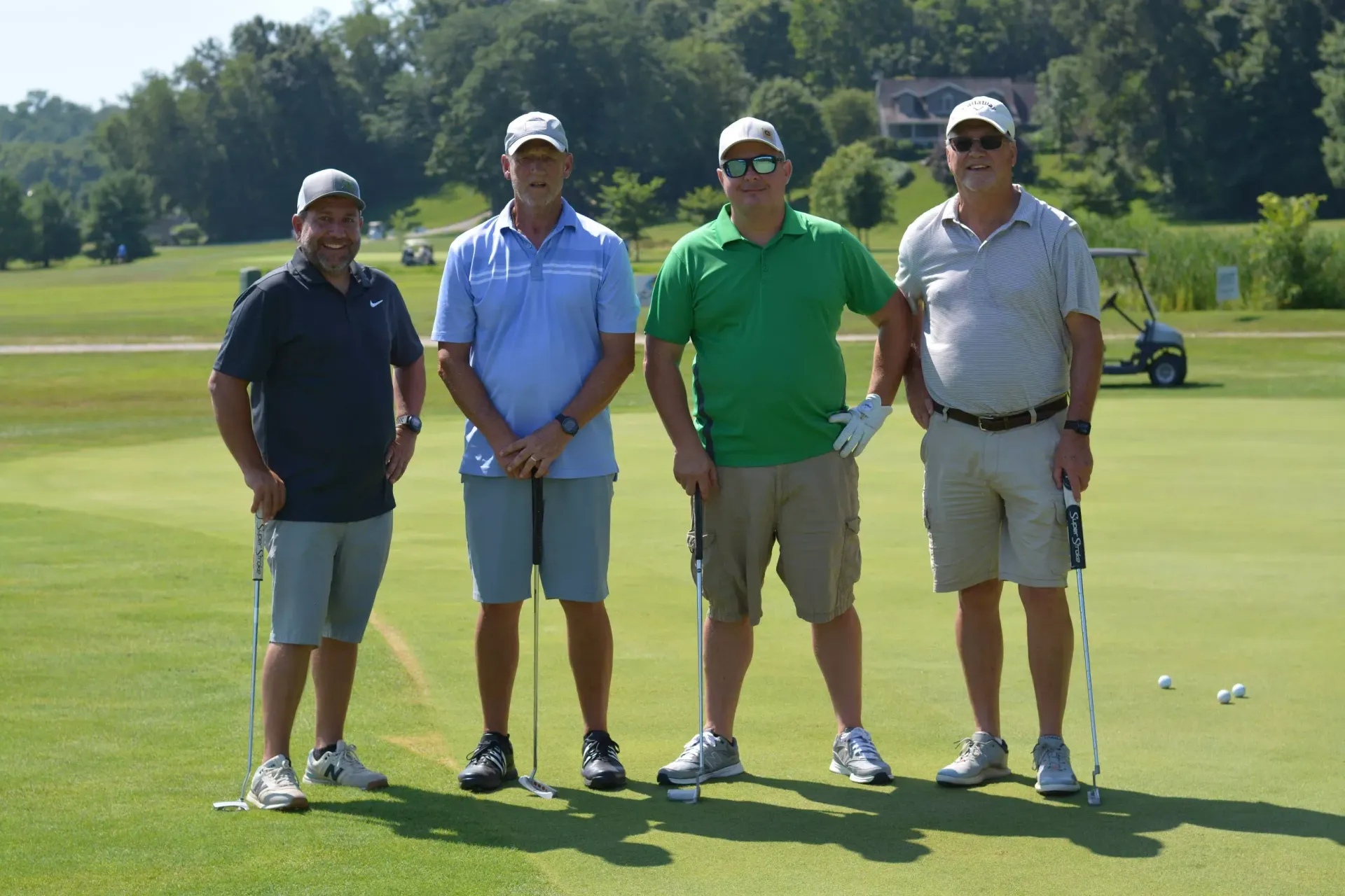 Four golfers posing on a sunny golf course with trees and hills in the background