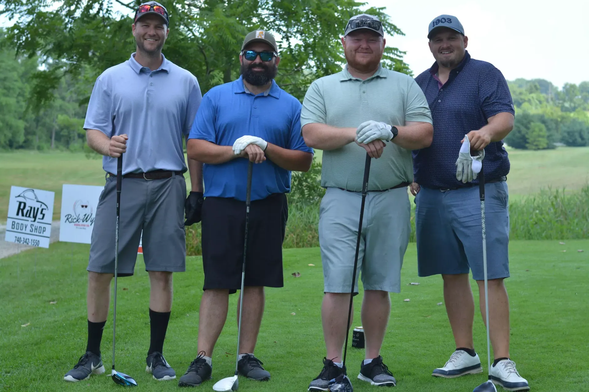 Four golfers posing on a green fairway, holding clubs and wearing gloves after a round.